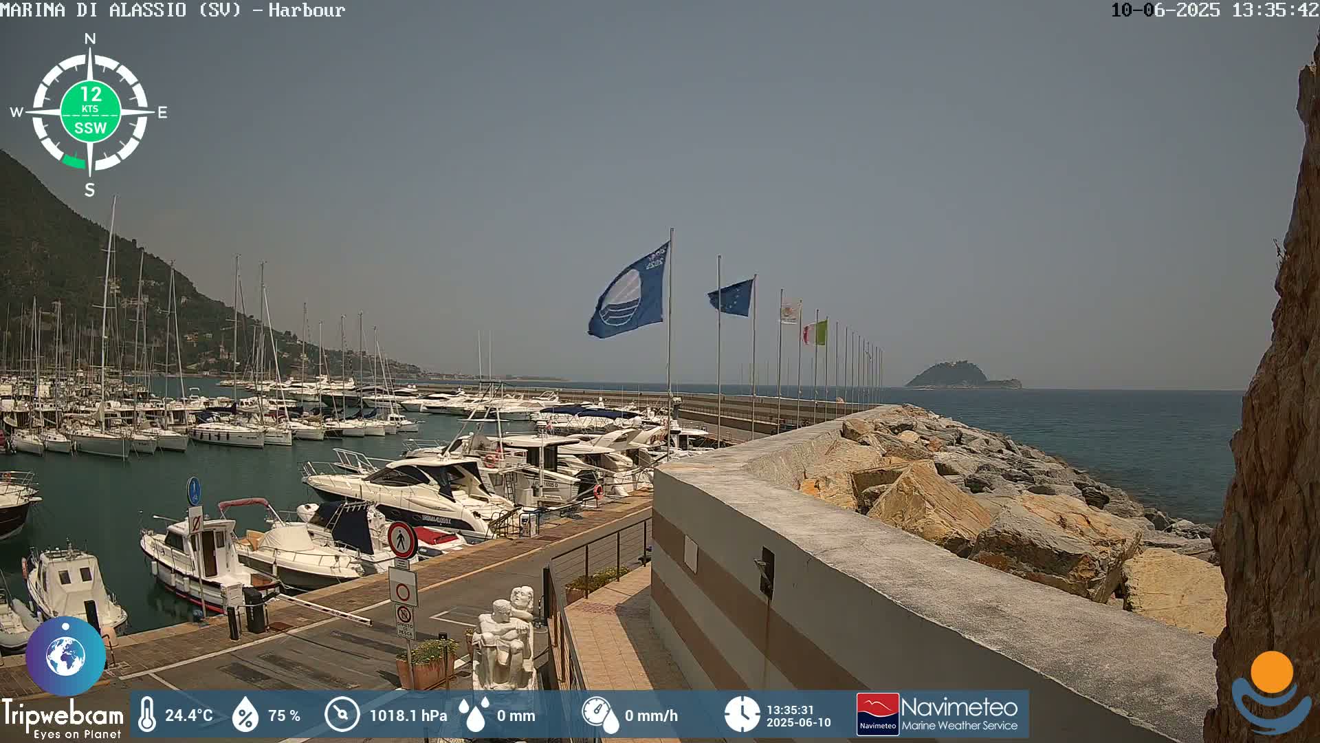 A harbor filled with numerous boats is situated beside a rocky shoreline on a sunny day with clear skies.