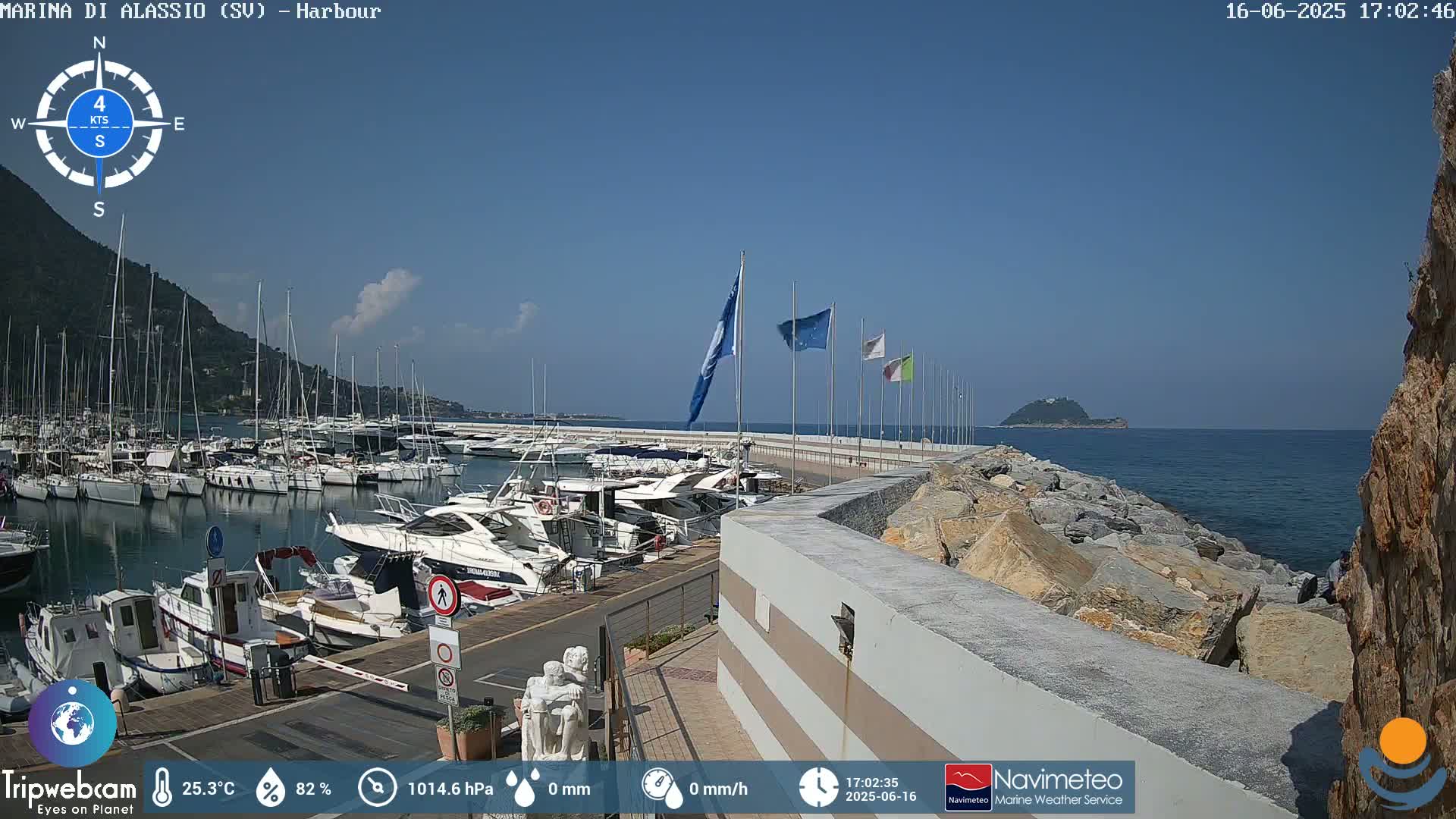A harbor filled with numerous boats is situated next to a rocky shoreline, under a mostly clear blue sky.