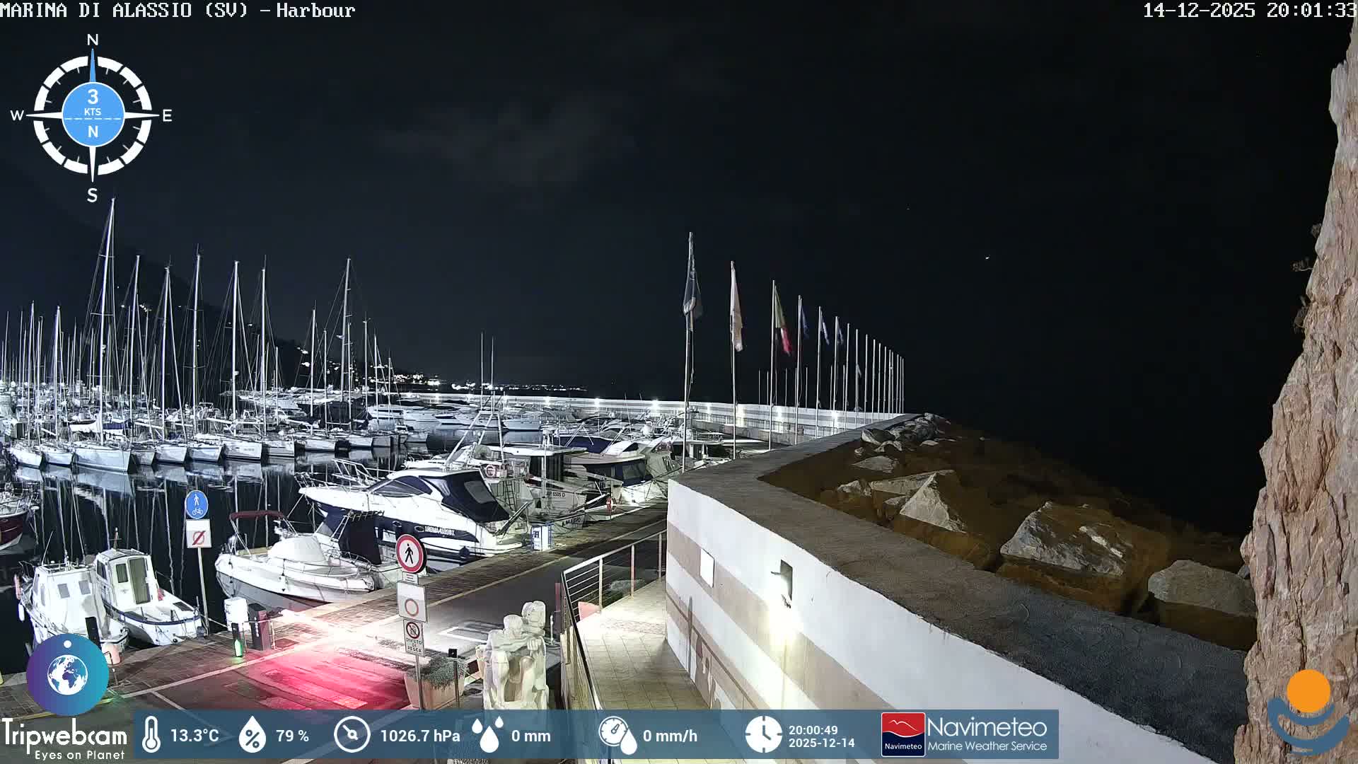 Under a heavy, overcast sky, a marina is filled with numerous boats and yachts alongside a wet pier and rocky breakwater, with distant hills and an island visible across choppy waters.