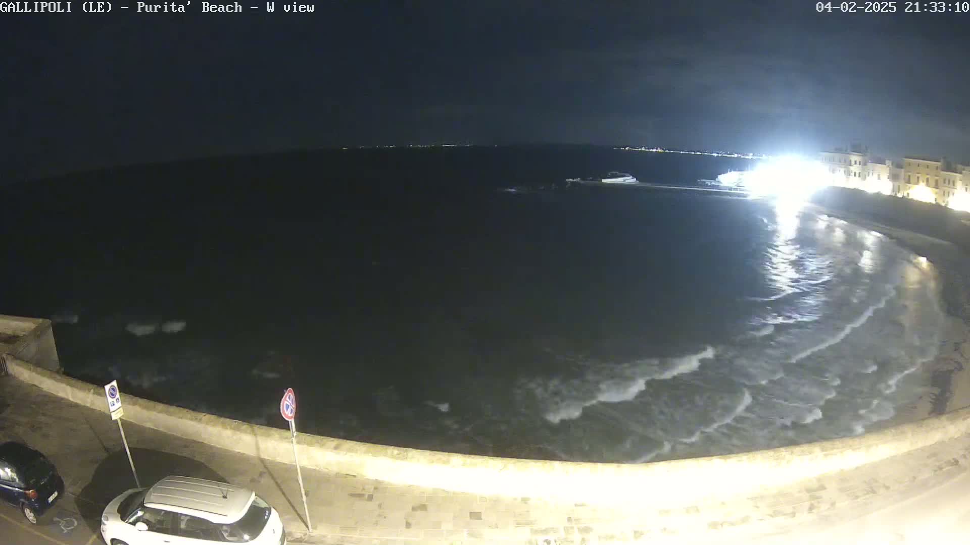 A nighttime, overhead view of a beach with gently lapping waves under a dark sky.