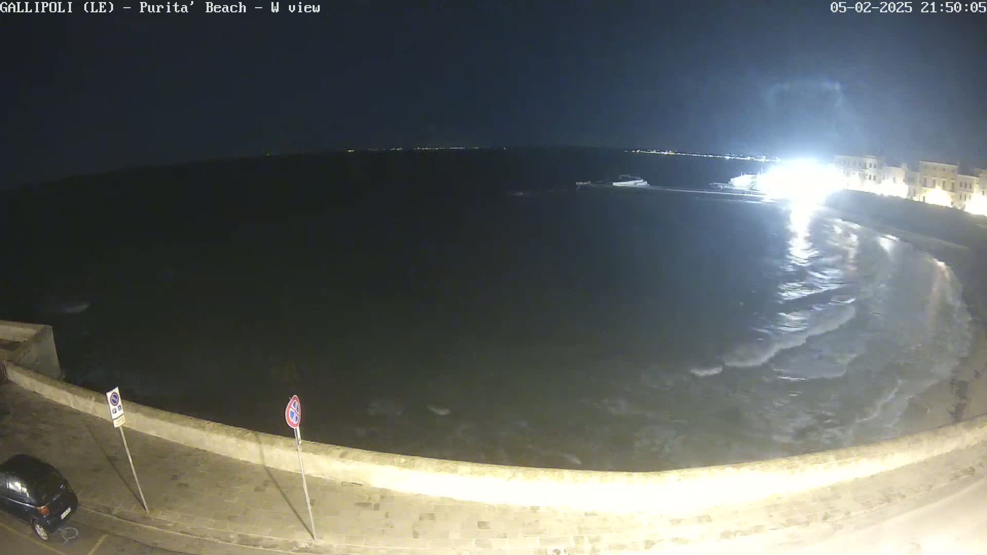 A nighttime view of a calm sea lapping gently against a stone wall, with small waves visible near the shore.