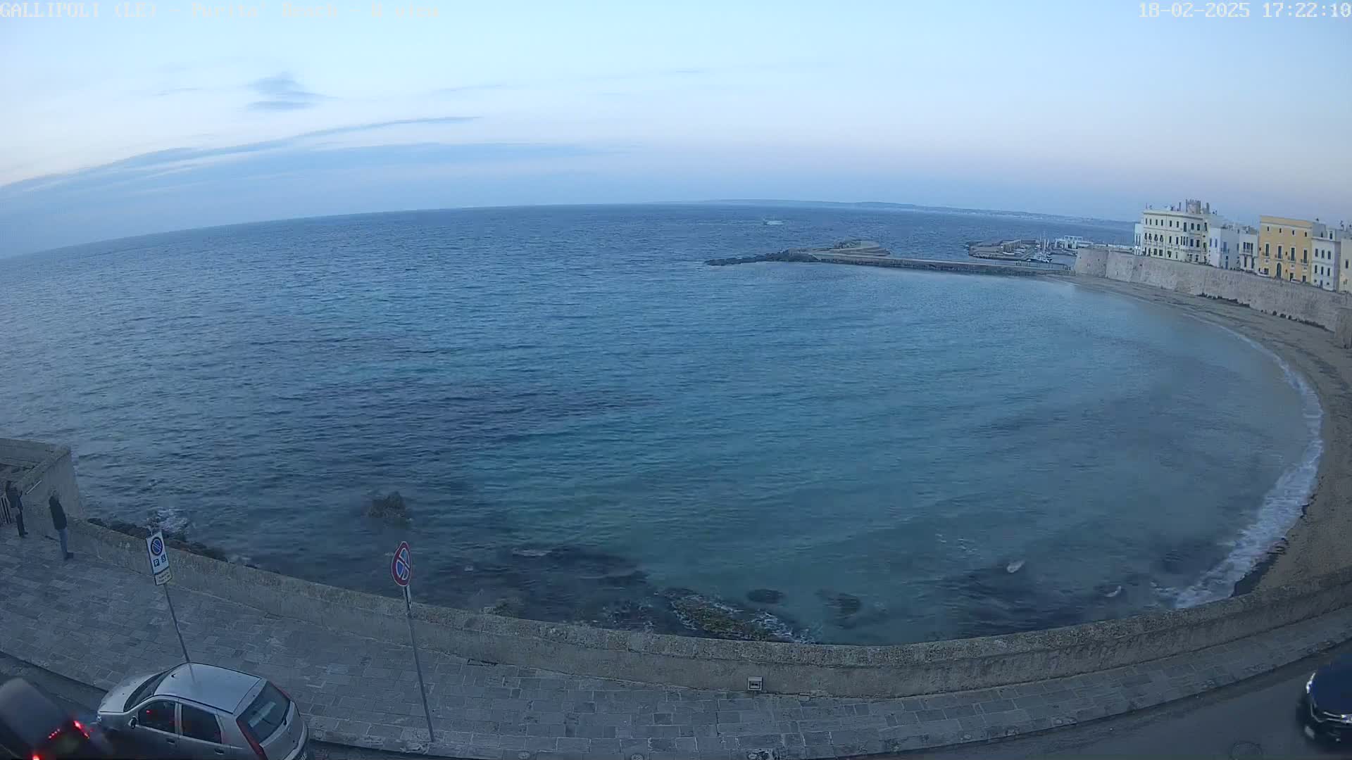A calm, blue sea curves around a coastal town under a clear, twilight sky.