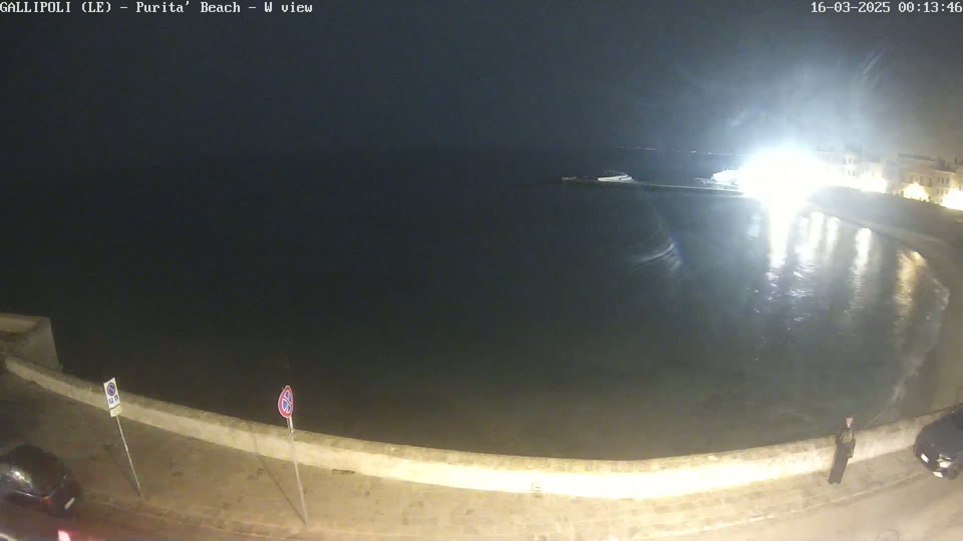 A nighttime view of a calm body of water next to a stone wall, with some lights visible in the distance.