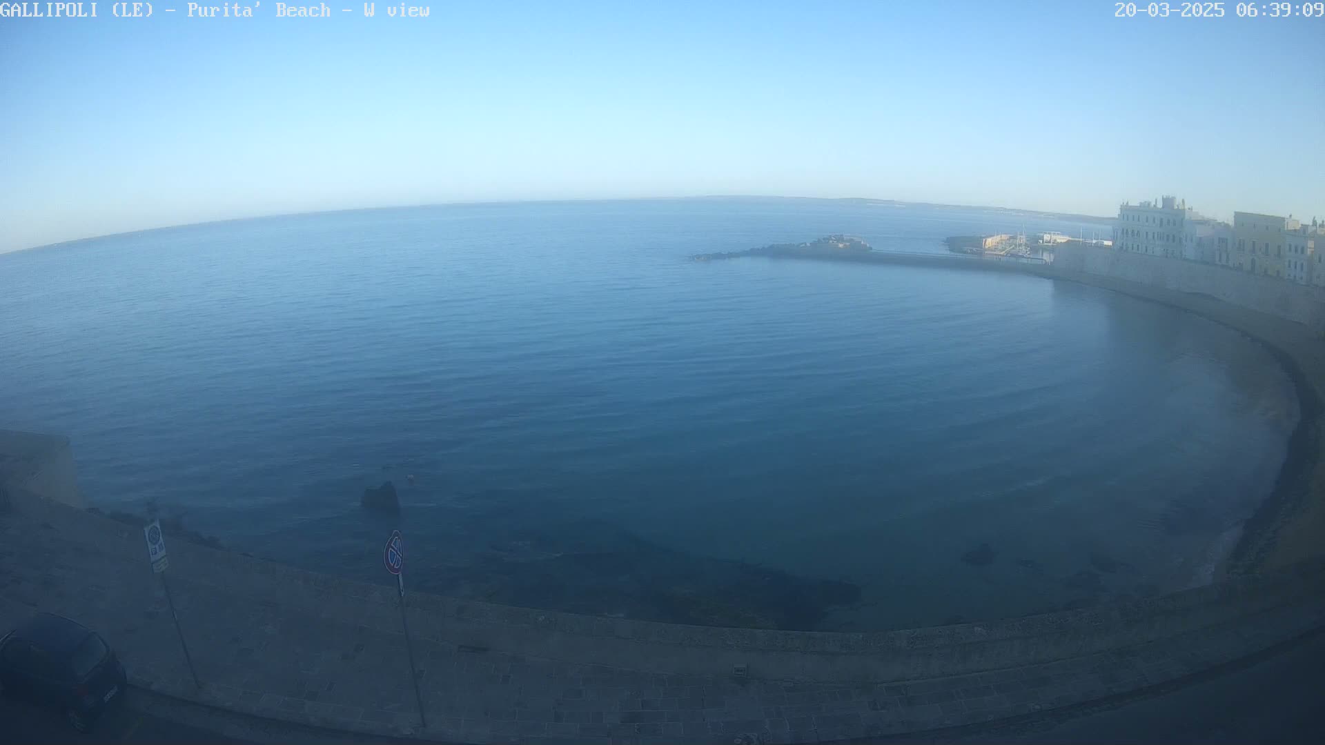 A calm, blue sea curves around a coastal town on a clear, sunny morning.