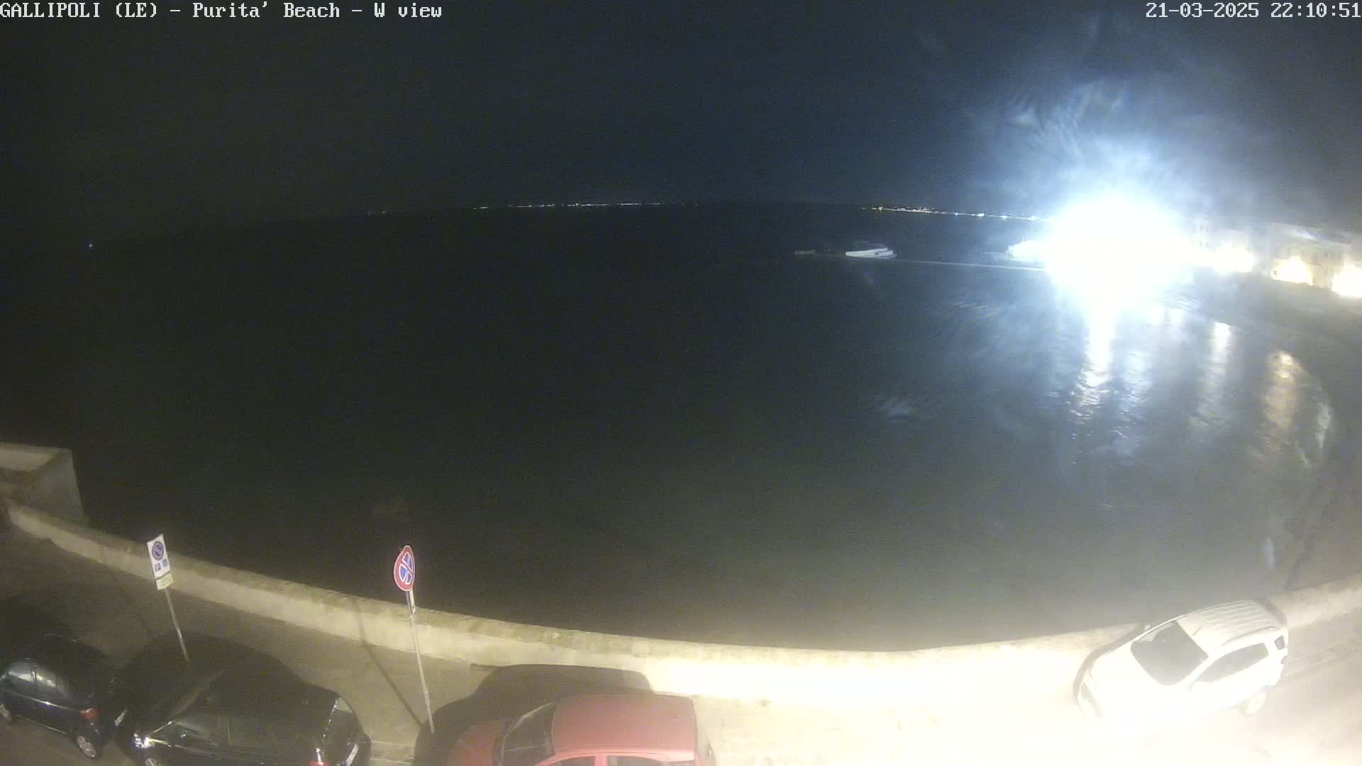 A nighttime view of a dark body of water with parked cars along a shoreline under a clear sky.