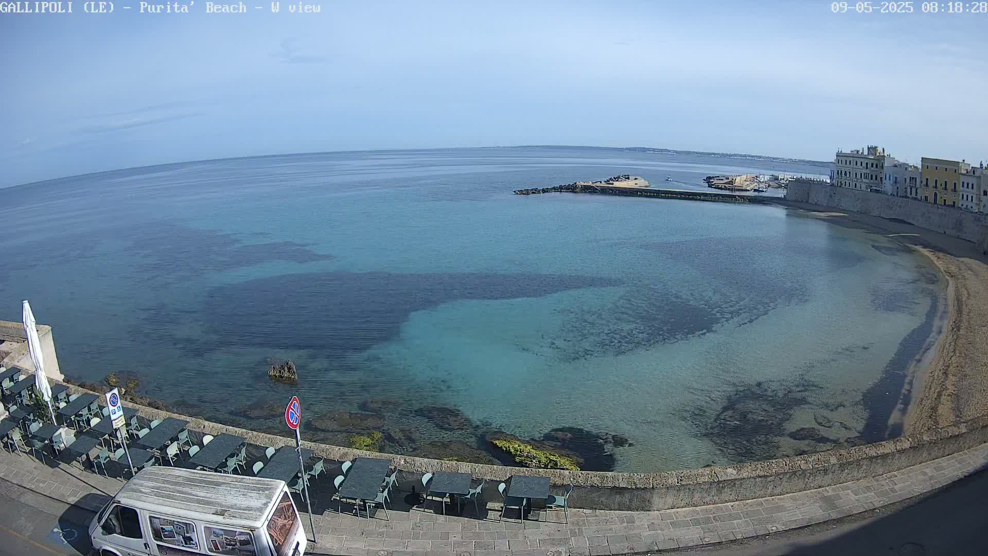 A clear, sunny day shows a calm, shallow, turquoise bay with a sandy beach curving around a seaside town.
