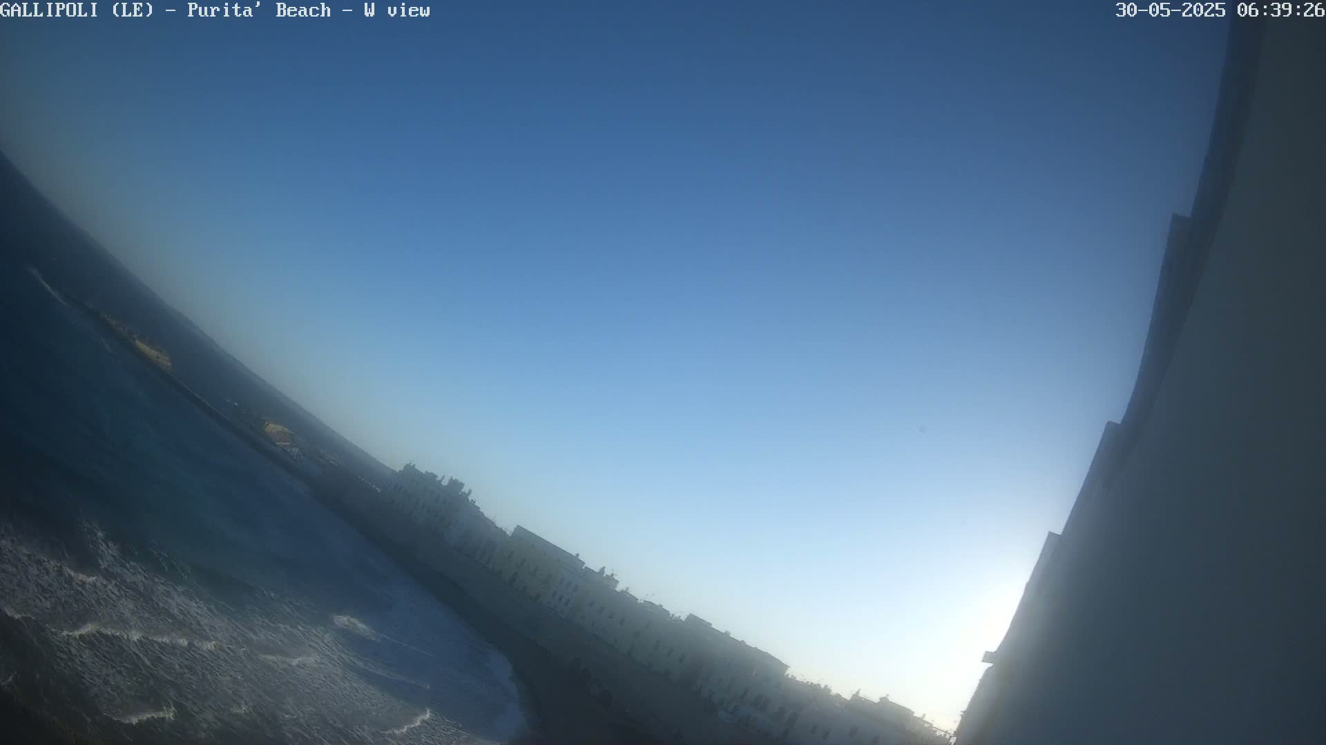 A clear blue sky is over a wavy ocean next to a line of buildings.