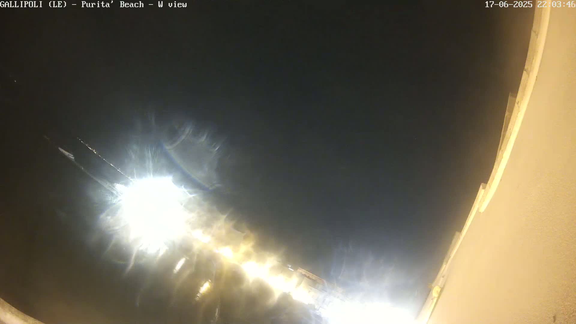 A nighttime view of a beach at sea level shows bright lights on the water and a dark sky.