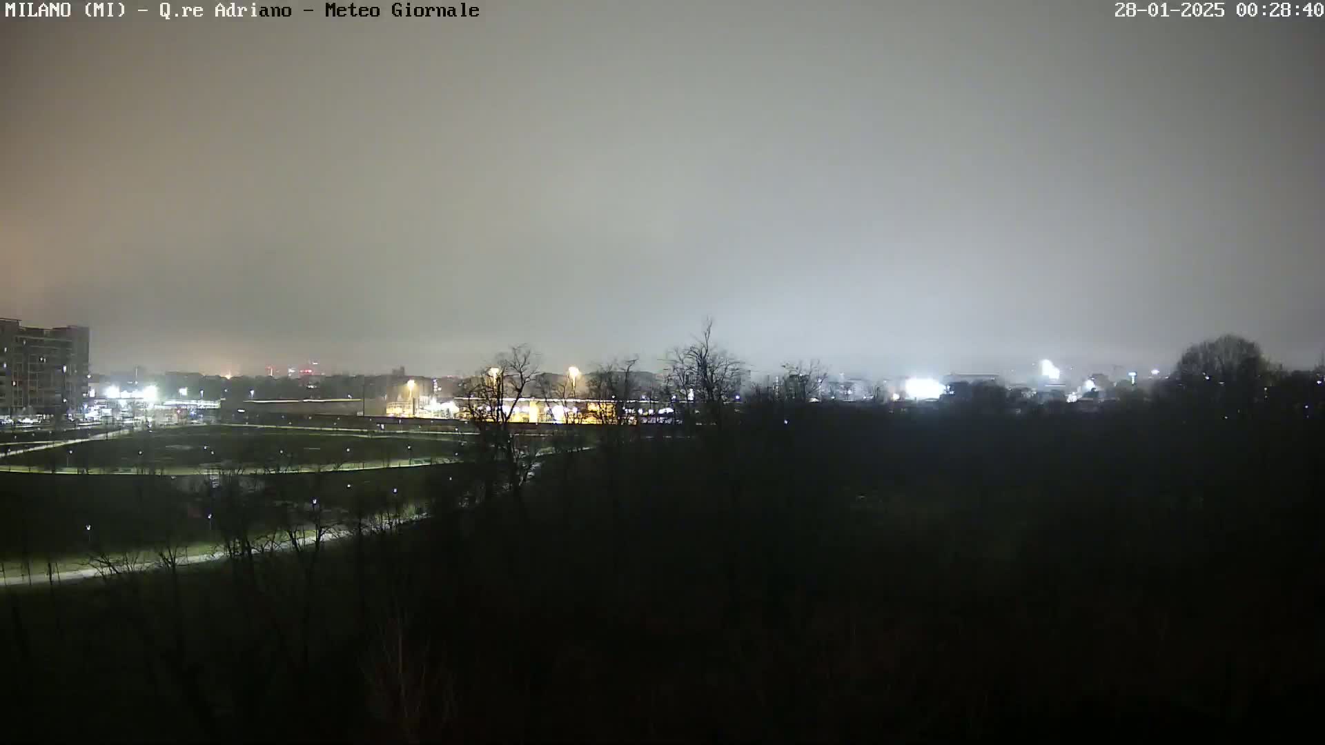 A nighttime view of a park and buildings under a hazy, overcast sky.