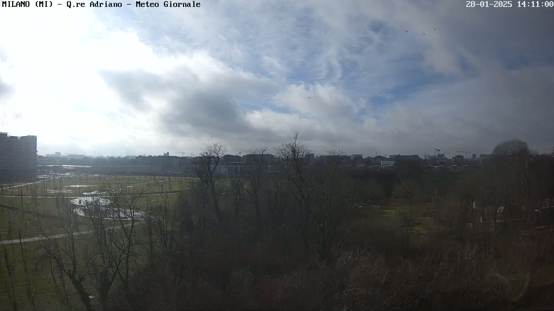 A partly cloudy day reveals a view of a park with bare trees and buildings in the distance.