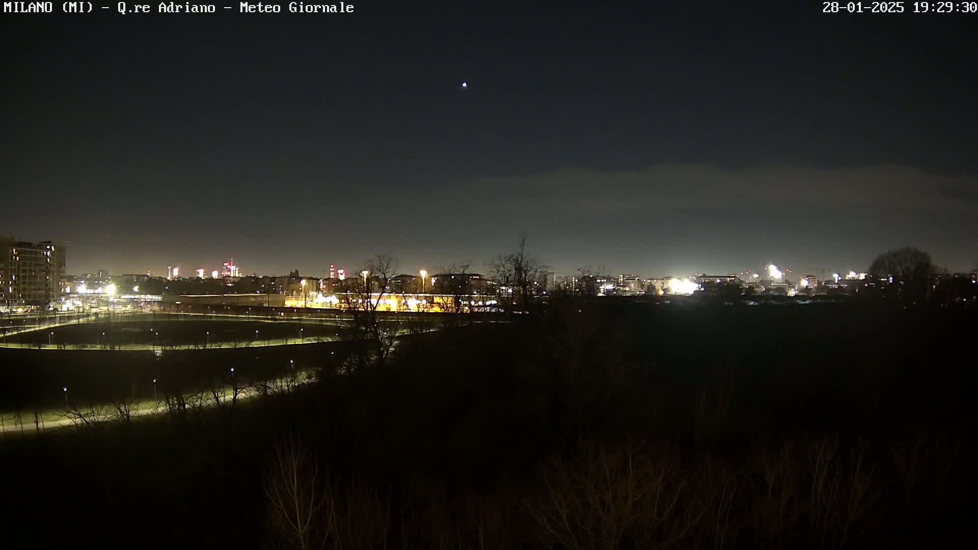 A nighttime view of a city skyline across a dark, sparsely lit park under a clear sky.