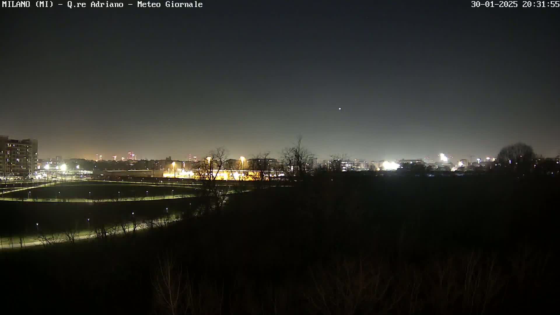A nighttime view of a city skyline across a dark, empty park with a clear, dark sky.