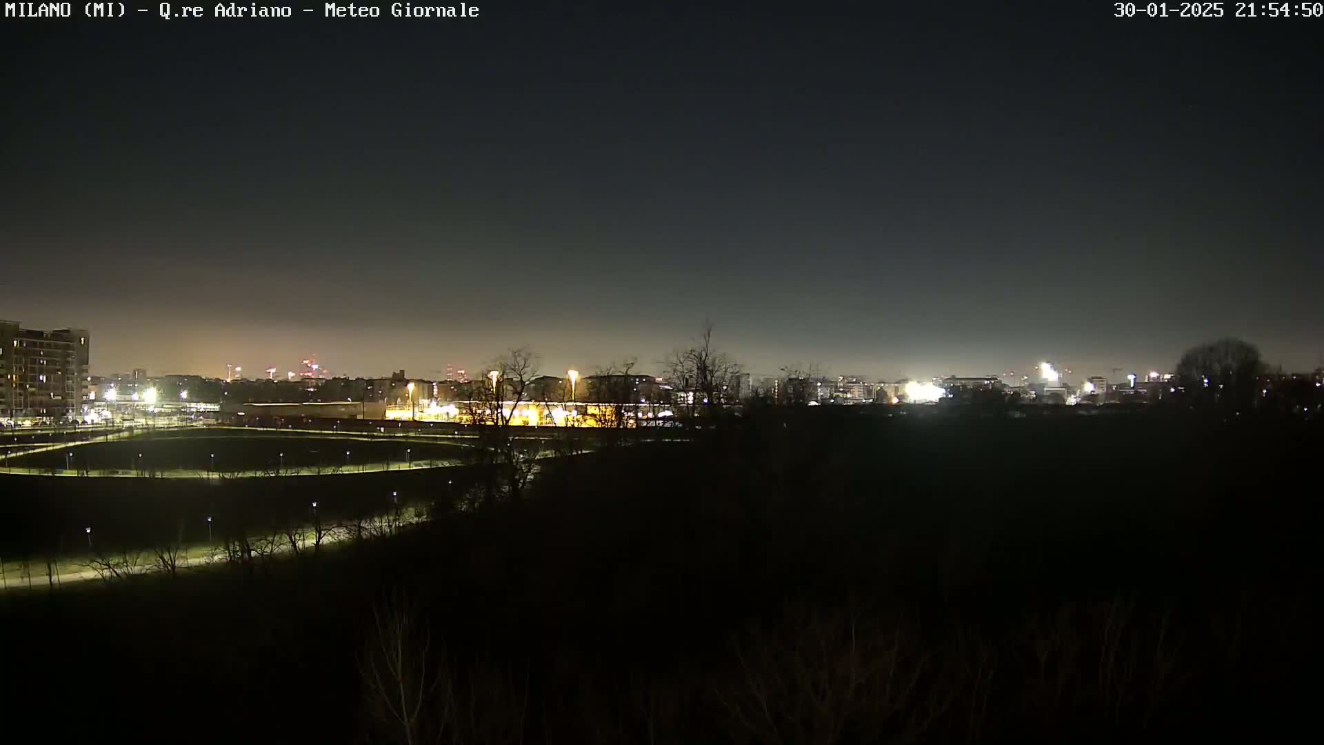 A nighttime view of a city skyline across a dark, sparsely vegetated area under a clear, dark sky.