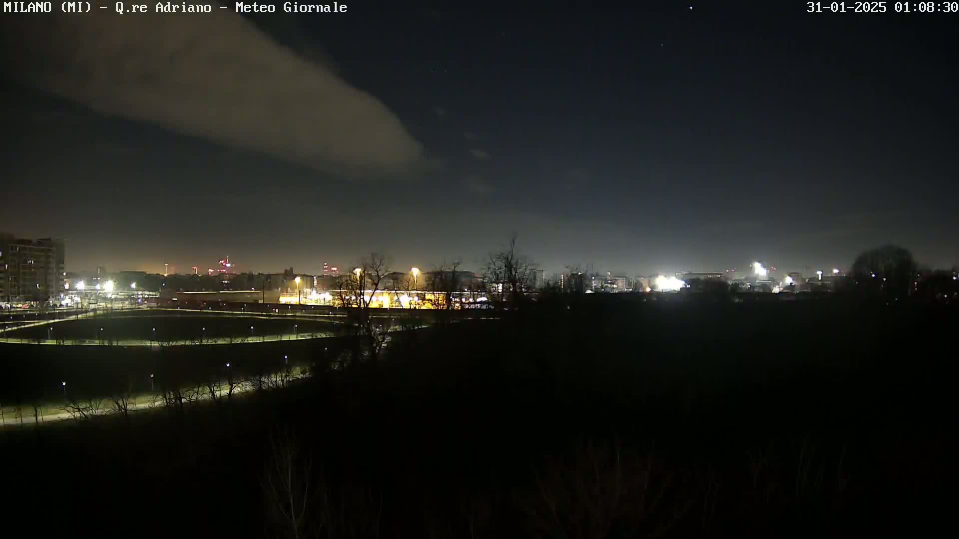 A nighttime view of a city skyline dimly lit under a mostly clear sky with a few clouds.