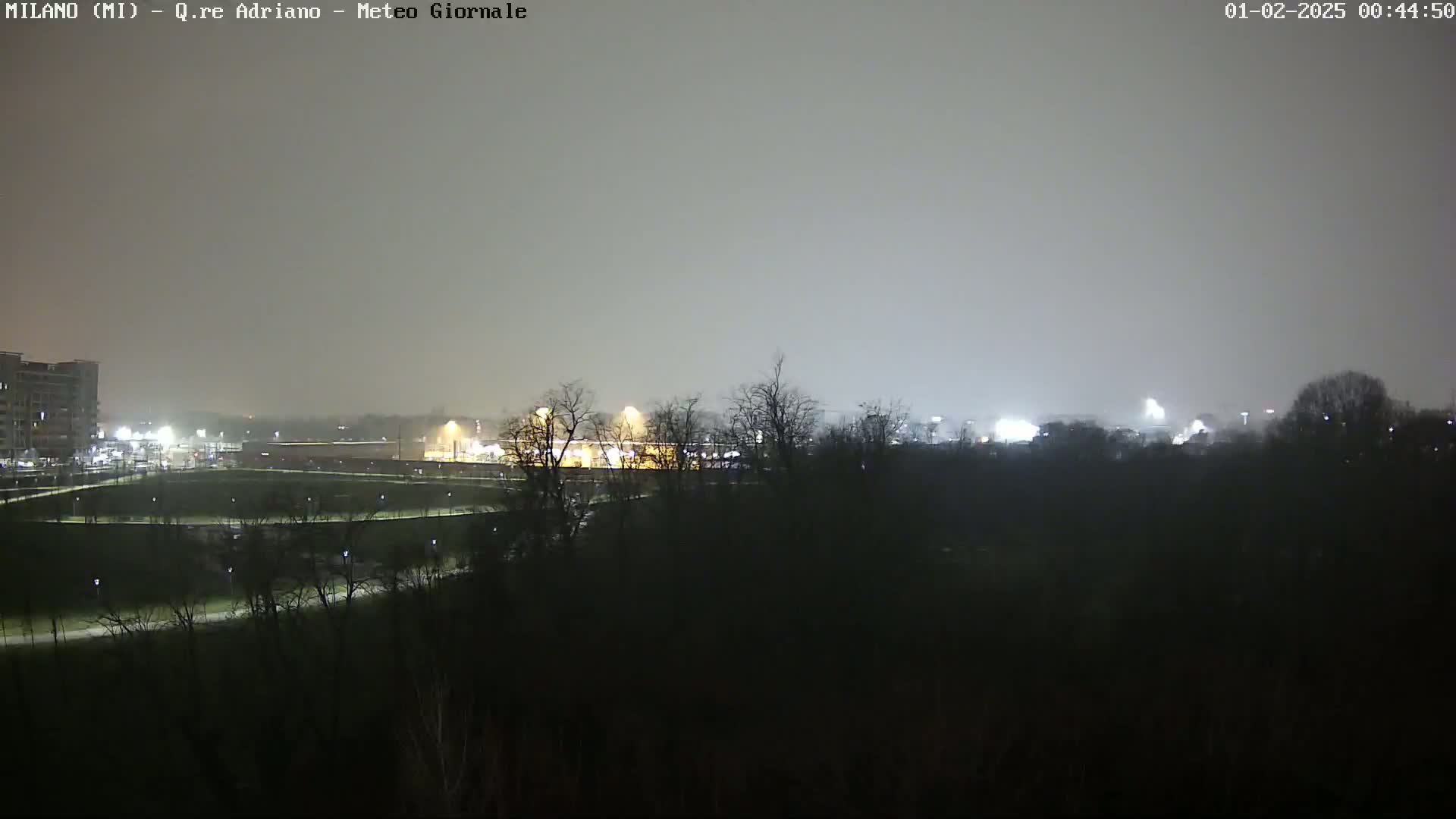 A nighttime view of a city park and surrounding buildings under a hazy, overcast sky.
