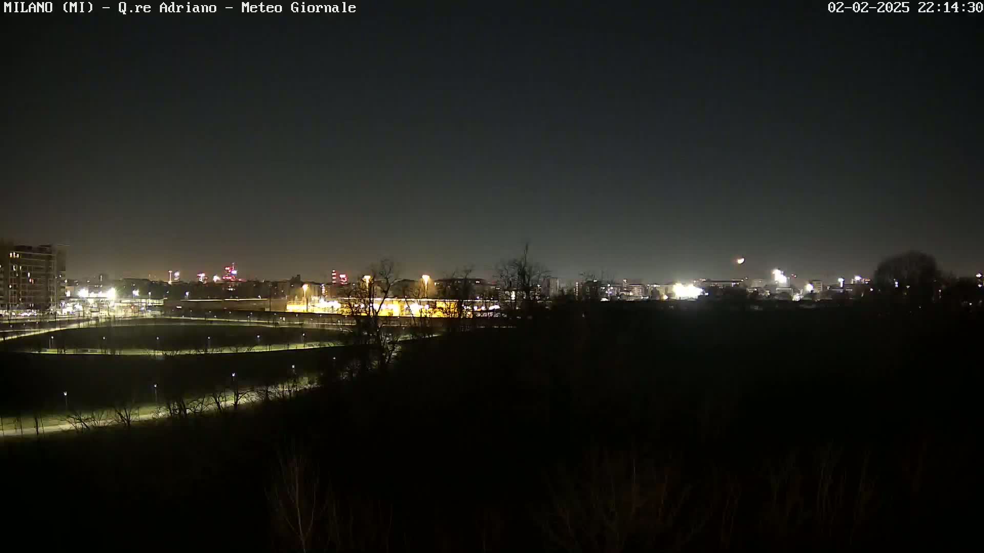 A nighttime view of a city skyline across a dark, sparsely lit park under a clear, dark sky.