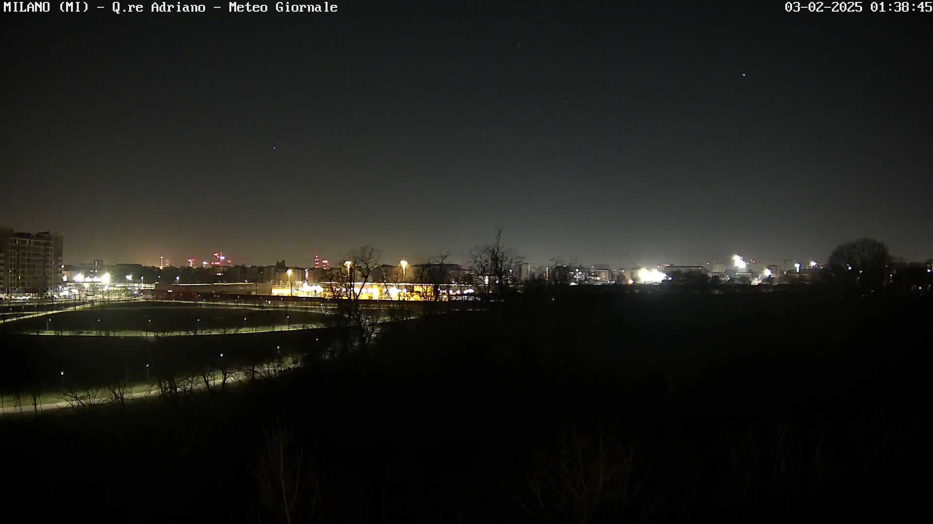 A nighttime view of a city skyline across a dark expanse of land, illuminated by sparsely placed lights.