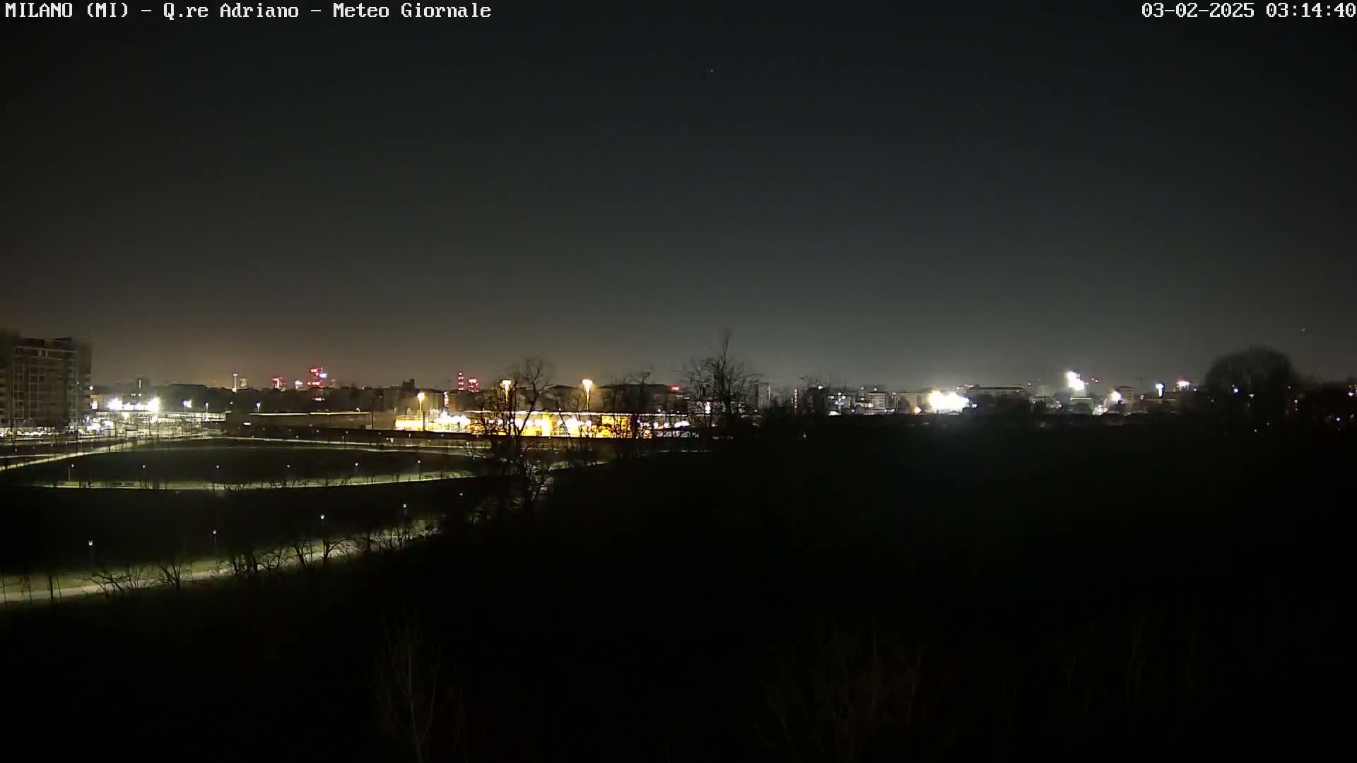A nighttime view of a city skyline across a dark, empty field under a clear, starlit sky.