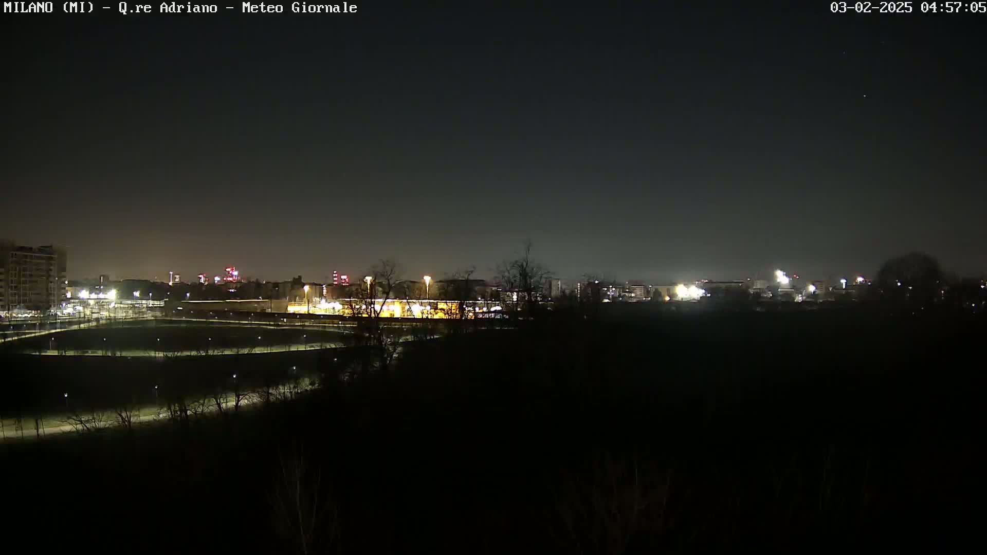 A nighttime view of a city skyline across a dark expanse of land, sparsely lit with streetlights.