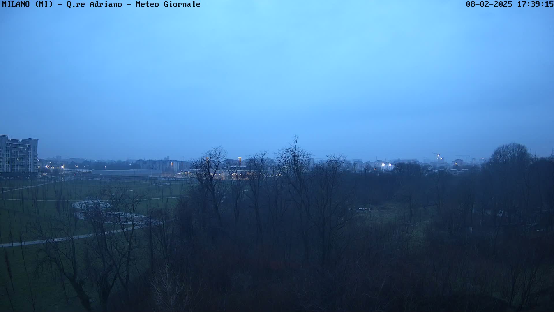 A twilight view shows a park with bare trees and distant buildings under a clear, dusky blue sky.