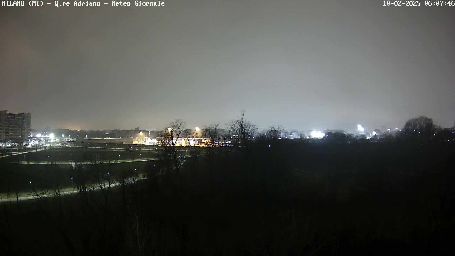 A nighttime view of a city park with buildings and lights in the distance under an overcast sky.