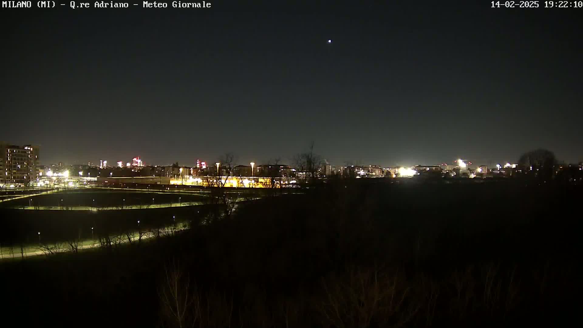 A nighttime view of a city skyline across a dark, sparsely lit park under a clear sky.