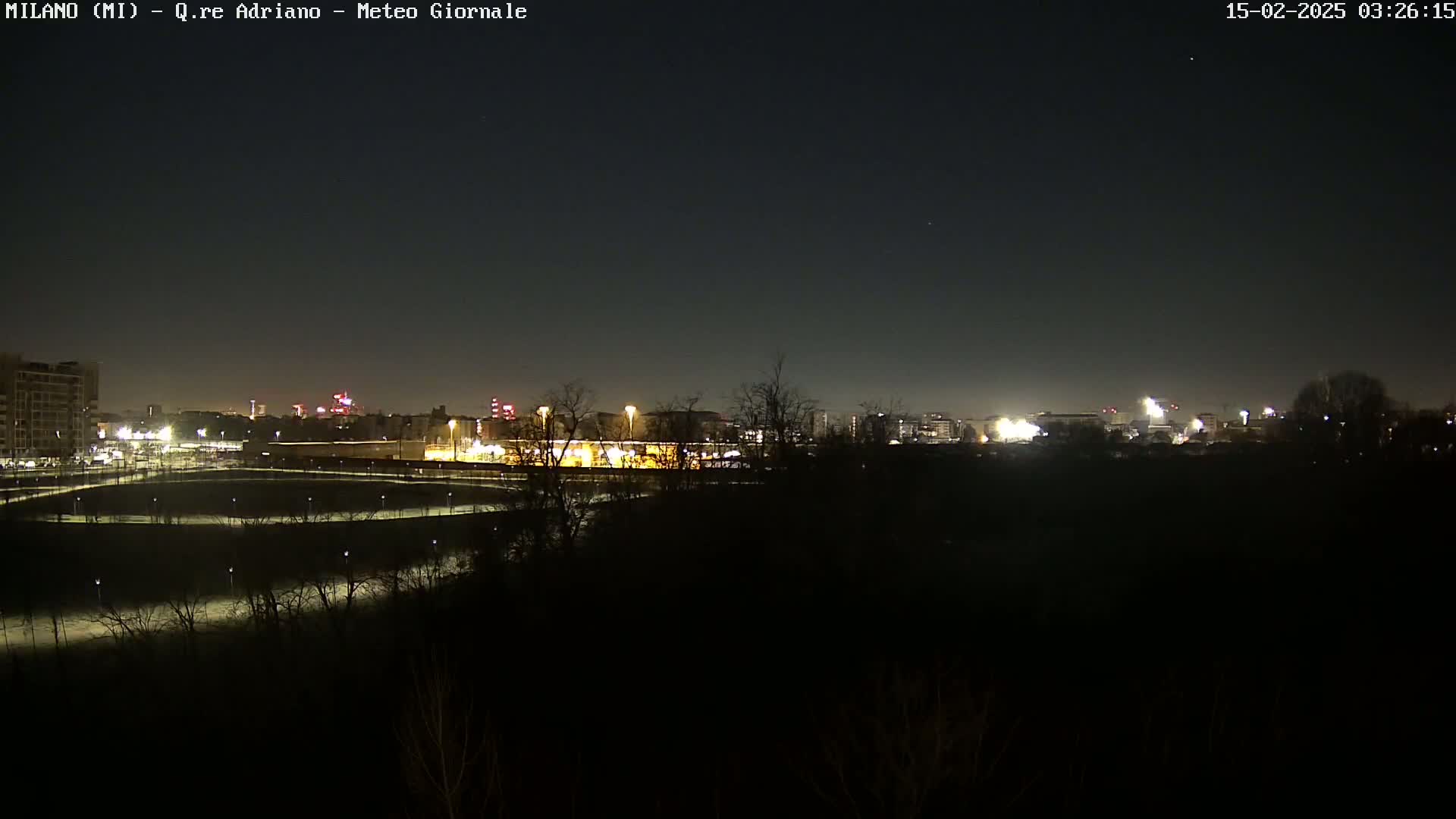 A nighttime view of a city skyline across a dark, sparsely vegetated area under a clear, dark sky.