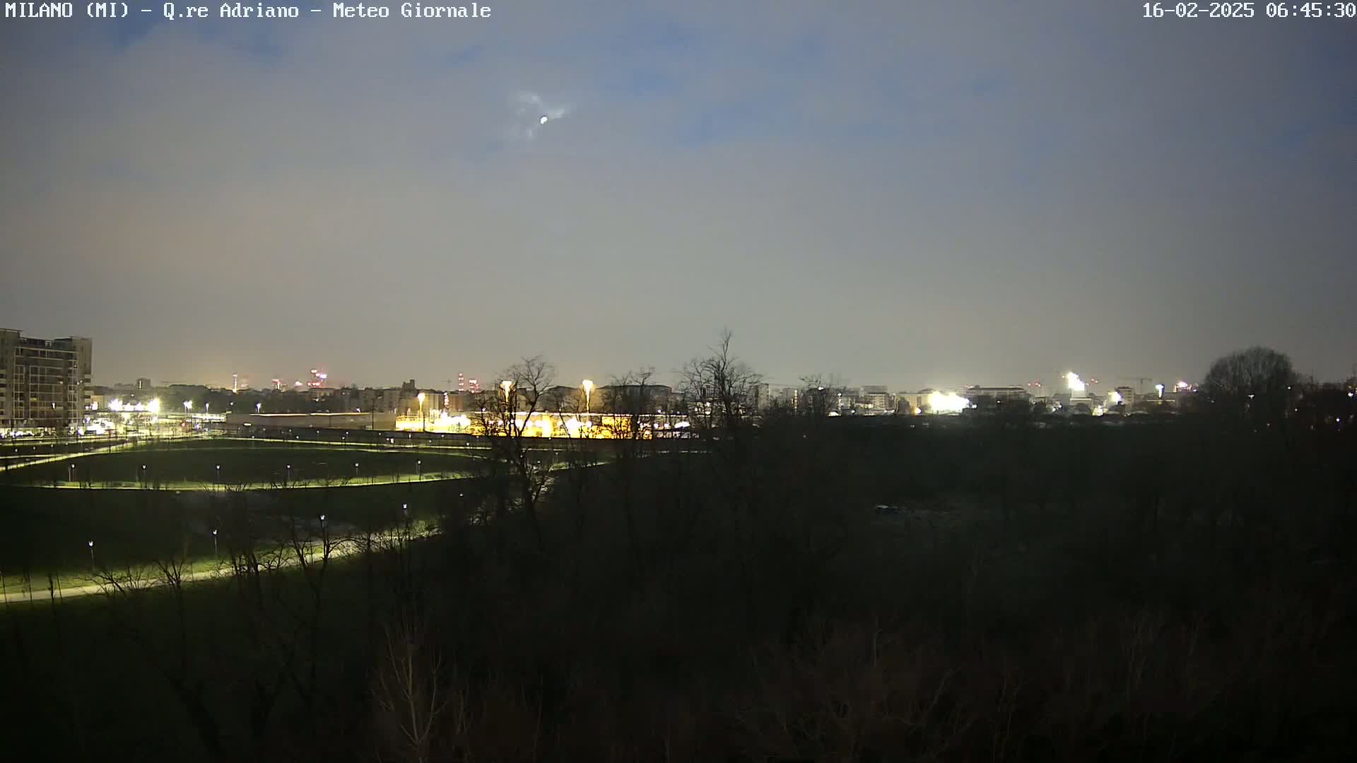A nighttime view of a city skyline across a dark, tree-lined park under a dusky sky.