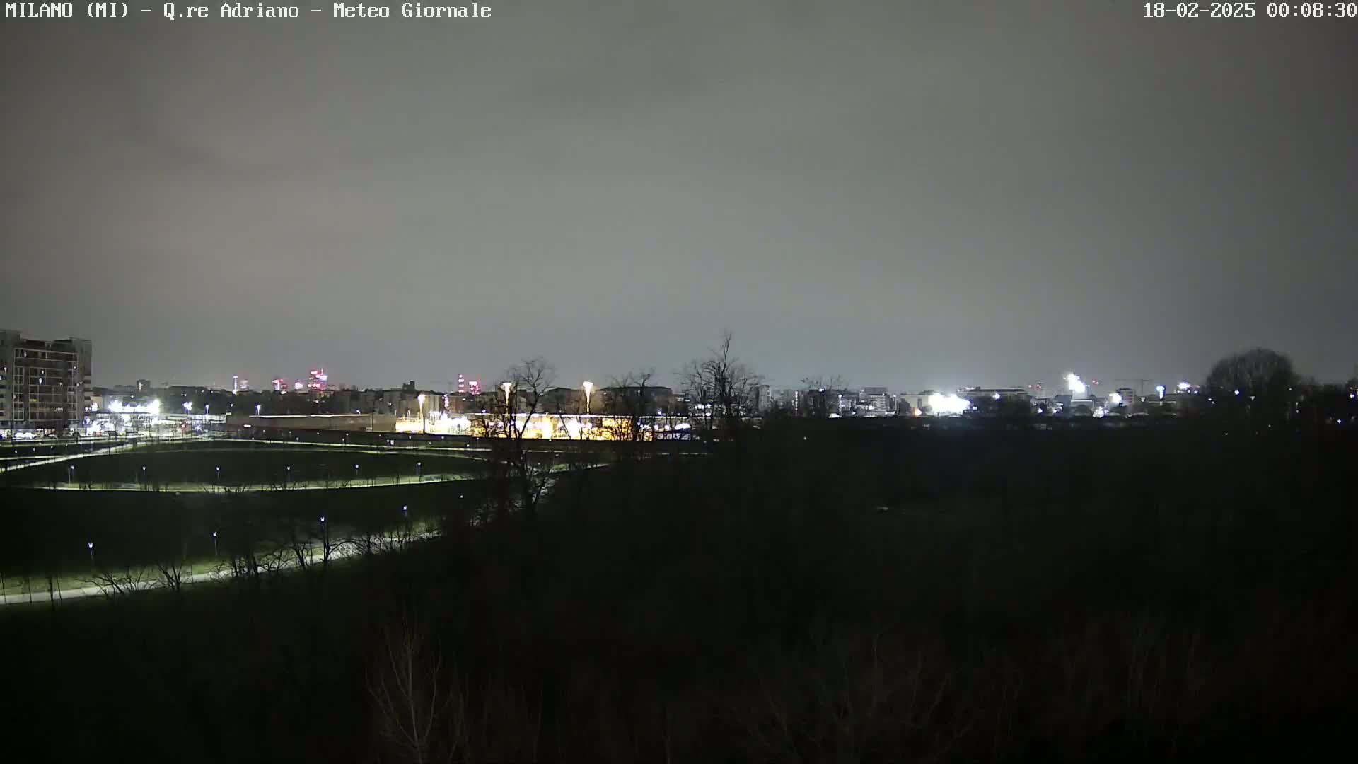 A nighttime view of a city skyline across a dark, empty park under an overcast sky.