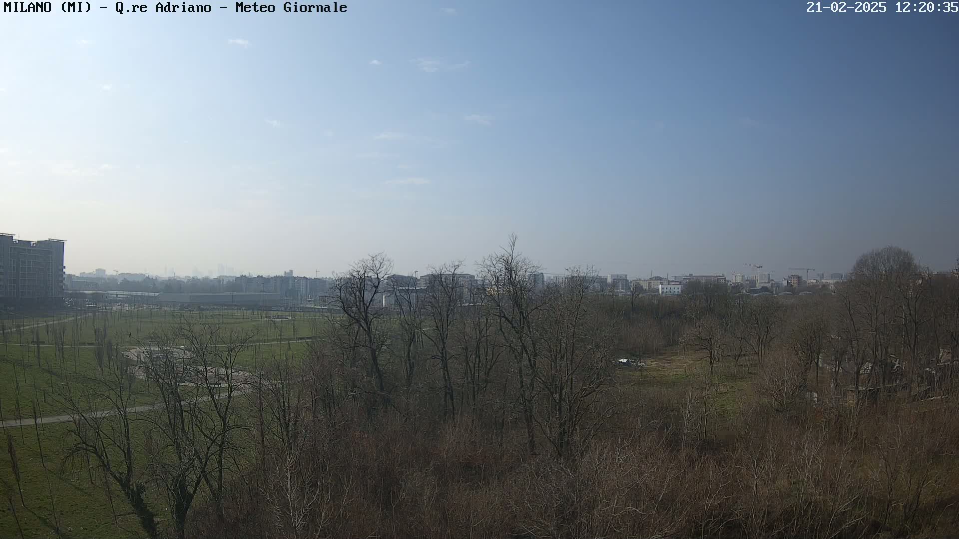 A clear, sunny day reveals a view of a park with bare trees, a grassy field, and buildings in the distance.