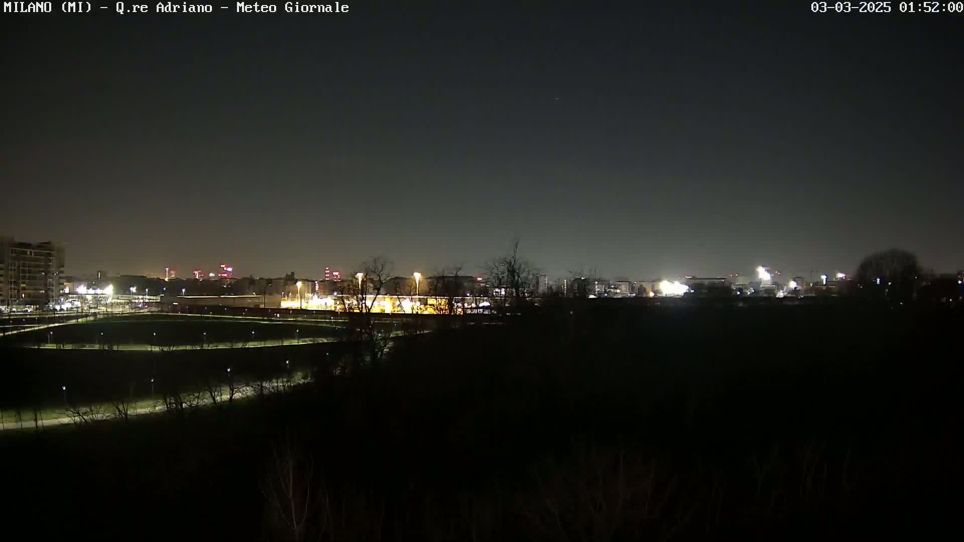 A nighttime view of a city skyline across a dark field, under a clear, dark sky.