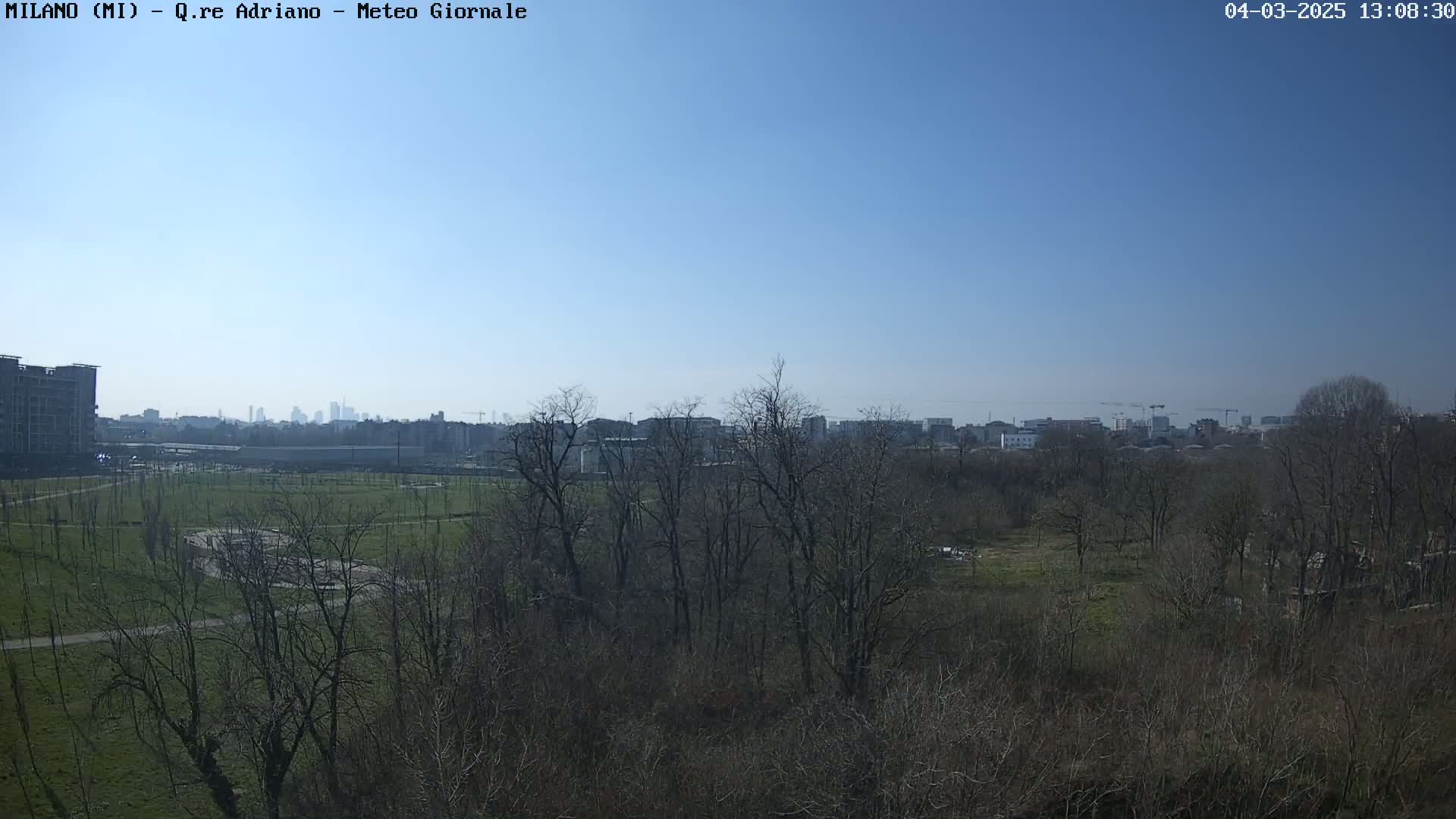 A clear, sunny day reveals a park with bare trees, a cityscape in the distance, and a partially visible building under construction to the left.