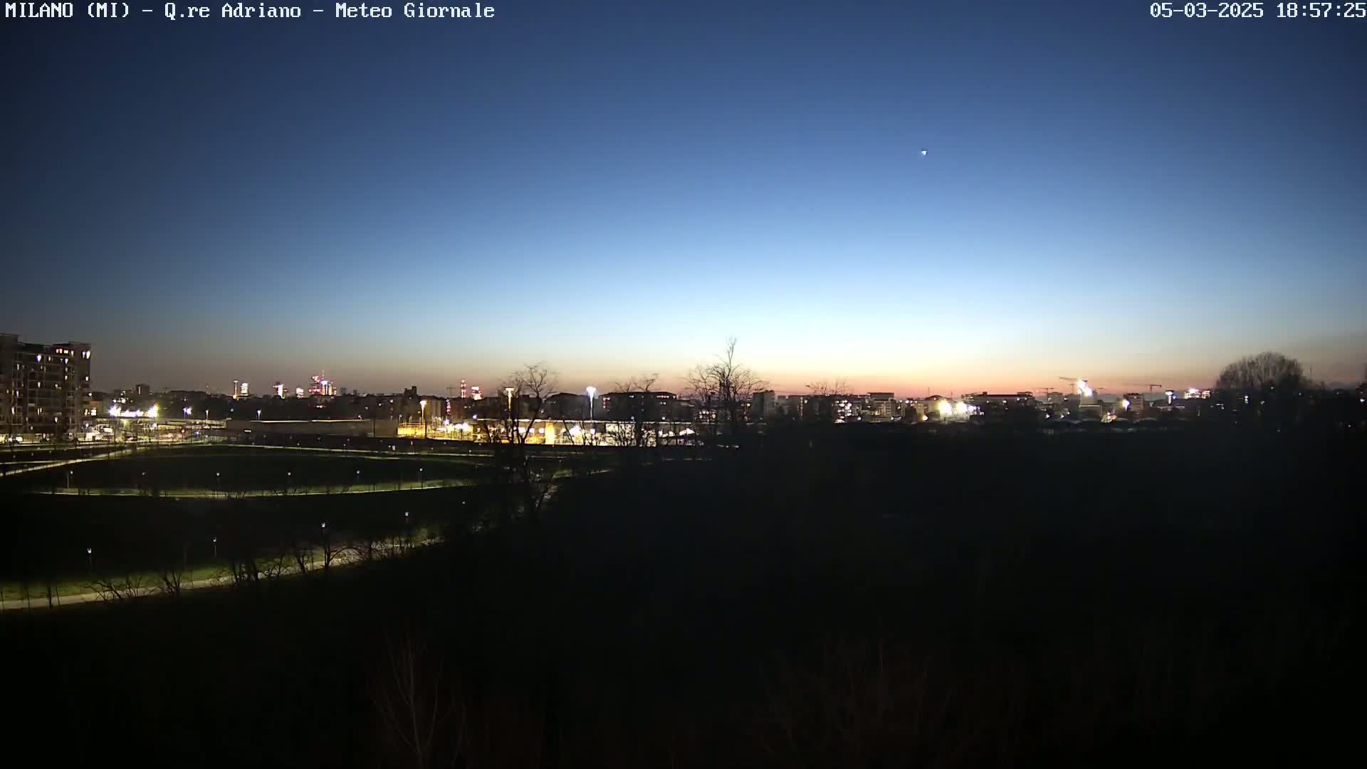 A twilight view of a city skyline at dusk, with a mostly clear sky and dimly lit park in the foreground.