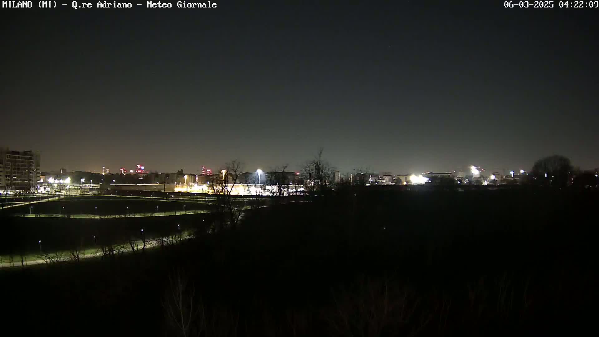 A nighttime view of a city skyline across a dark, sparsely vegetated area under a clear, dark sky.