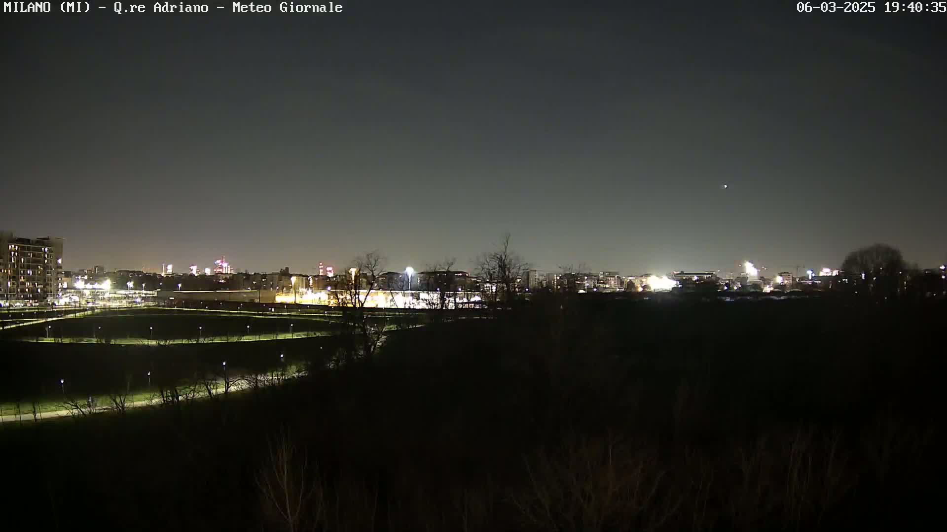 A nighttime view of a city skyline across a dark field, with a clear, dark sky.
