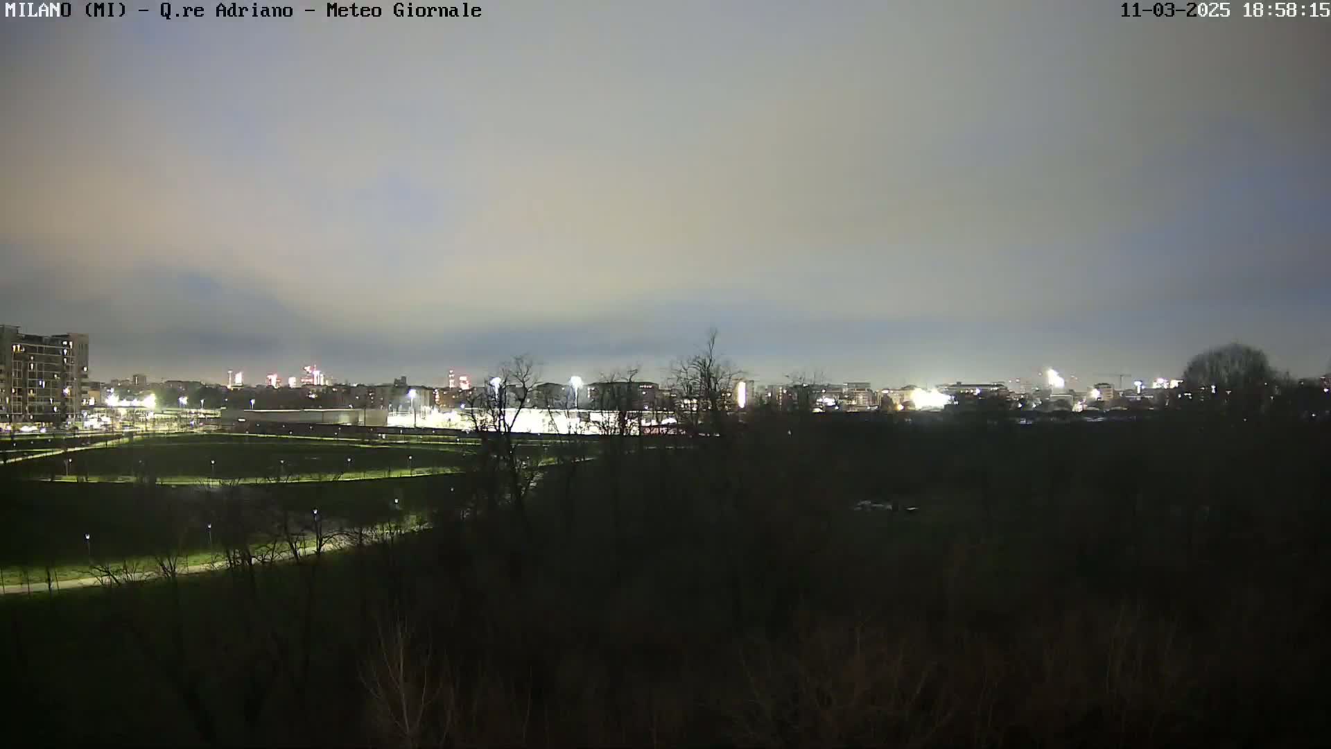 A nighttime view of a city skyline across a dark green field, under a dusky sky.