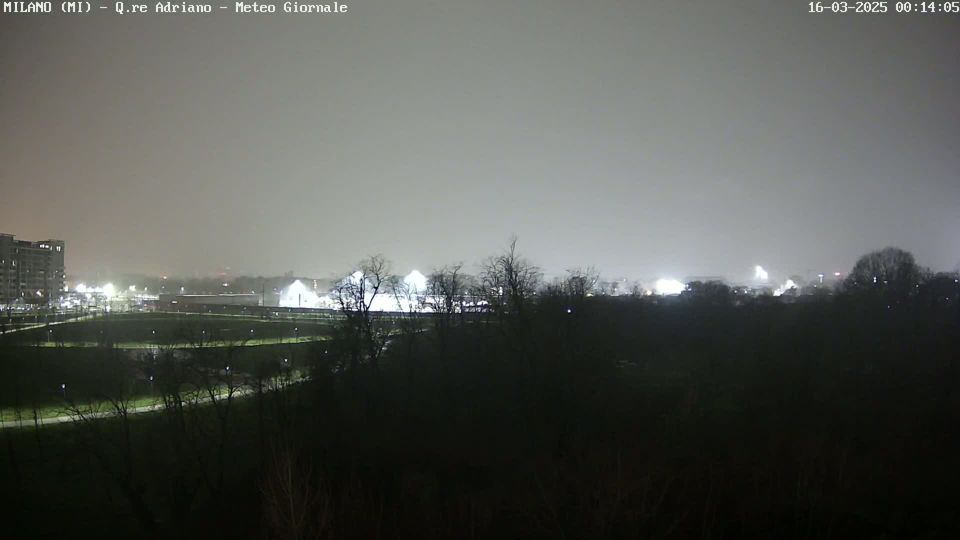A nighttime view of a dimly lit park and buildings under a hazy, overcast sky.