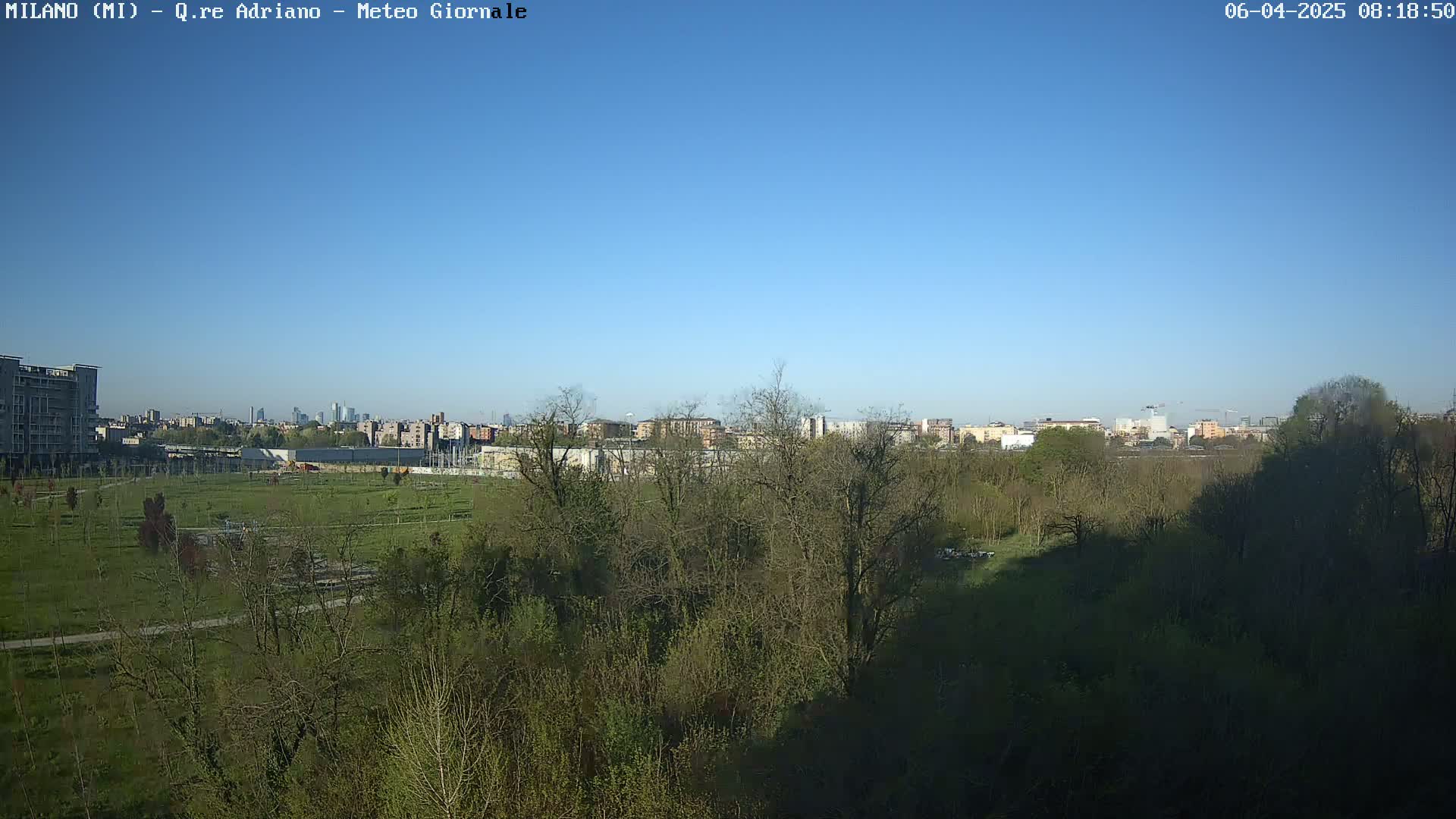 A clear blue sky overlooks a park with budding trees and a cityscape in the distance.