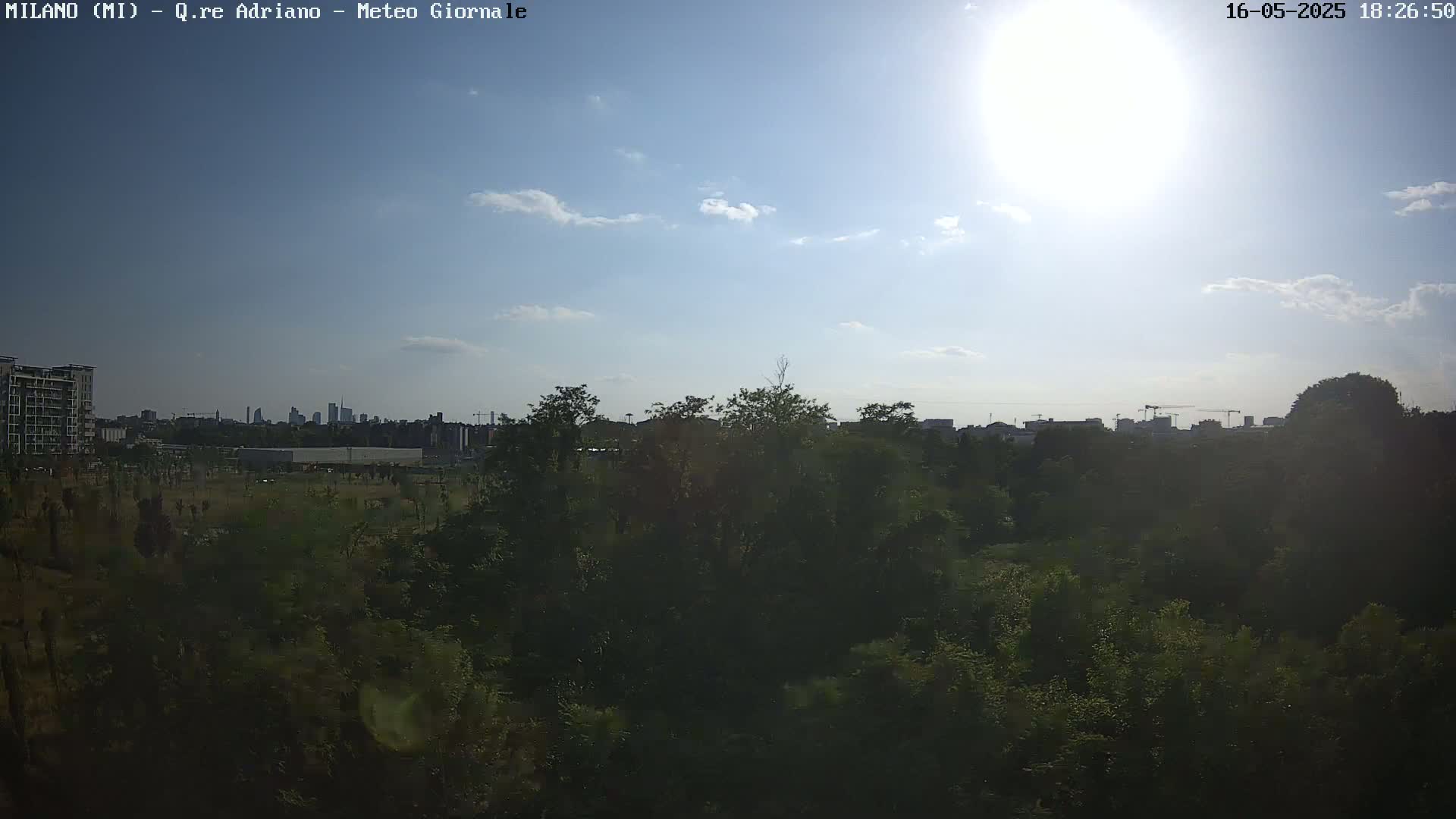 A mostly sunny sky with a few clouds overlooks a dense green landscape with a city skyline in the distance.