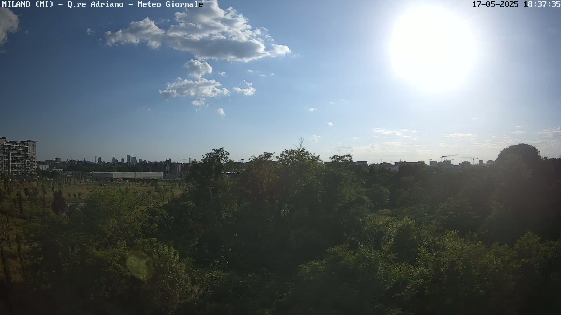 A sunny day with partly cloudy skies overlooks a lush green landscape and a distant cityscape.