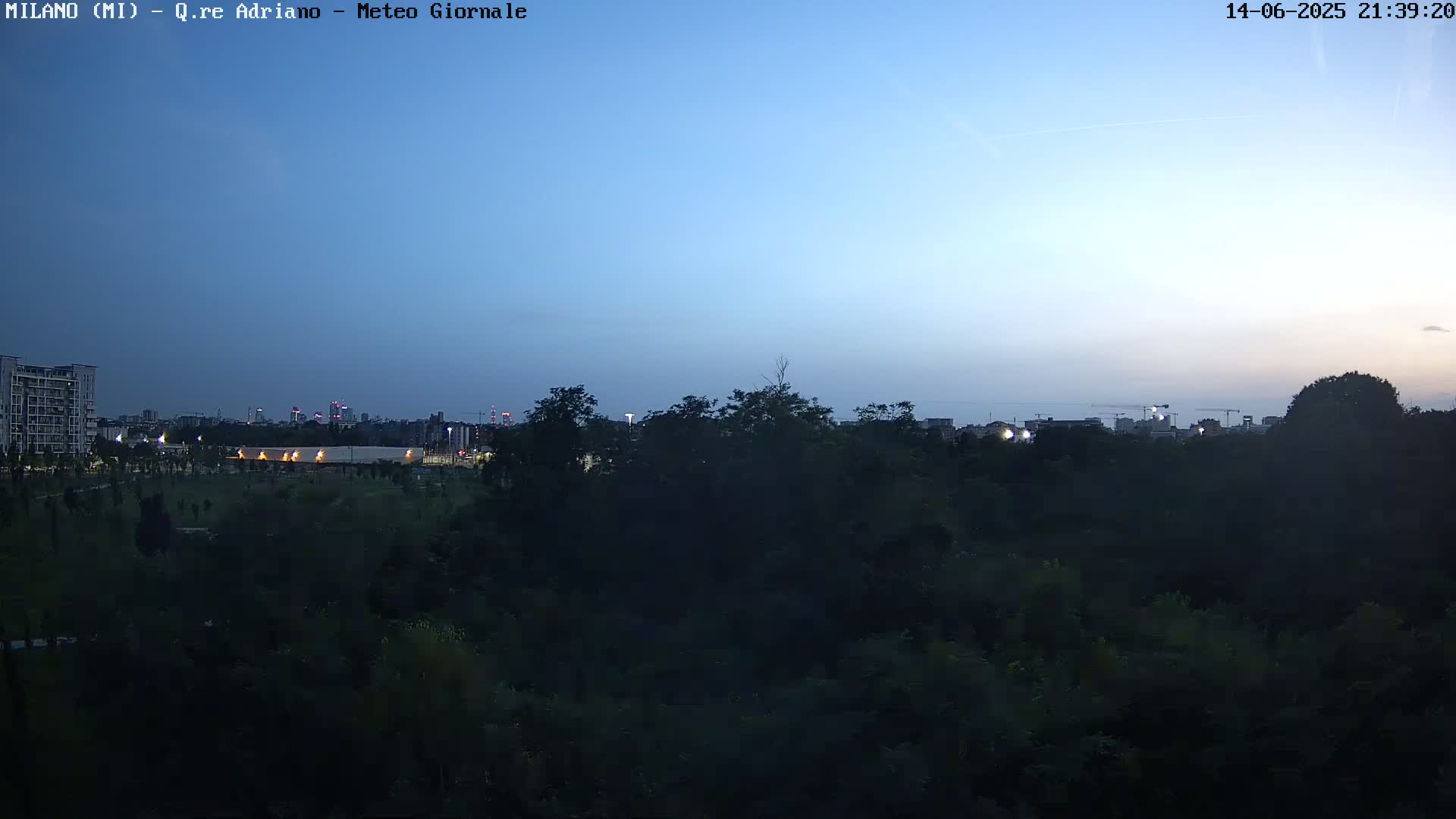 A mostly cloudy sky overlooks a dense, green park with a distant cityscape visible in the background.