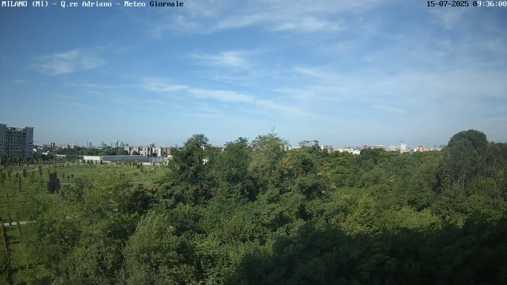 A mostly sunny sky overlooks a dense green park with a city skyline visible in the distance.