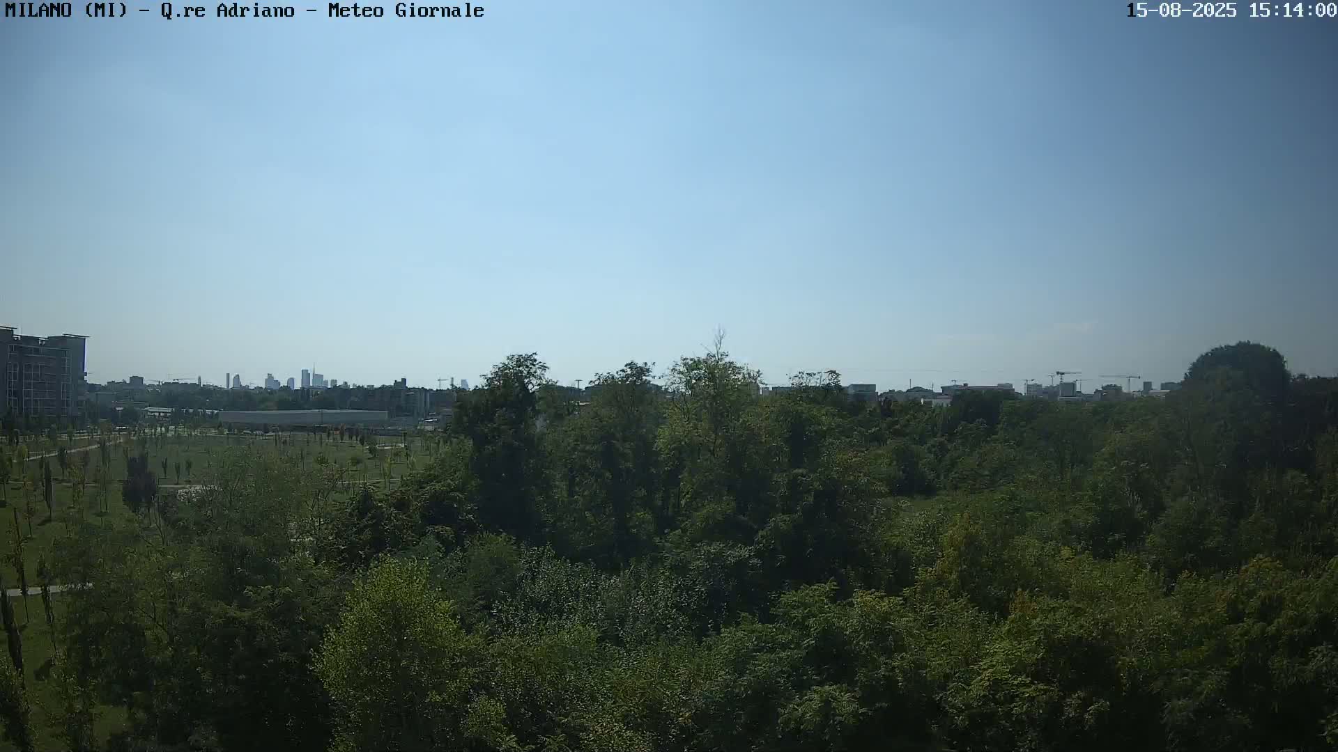 A mostly sunny sky overlooks a dense green park with a city skyline visible in the distance.