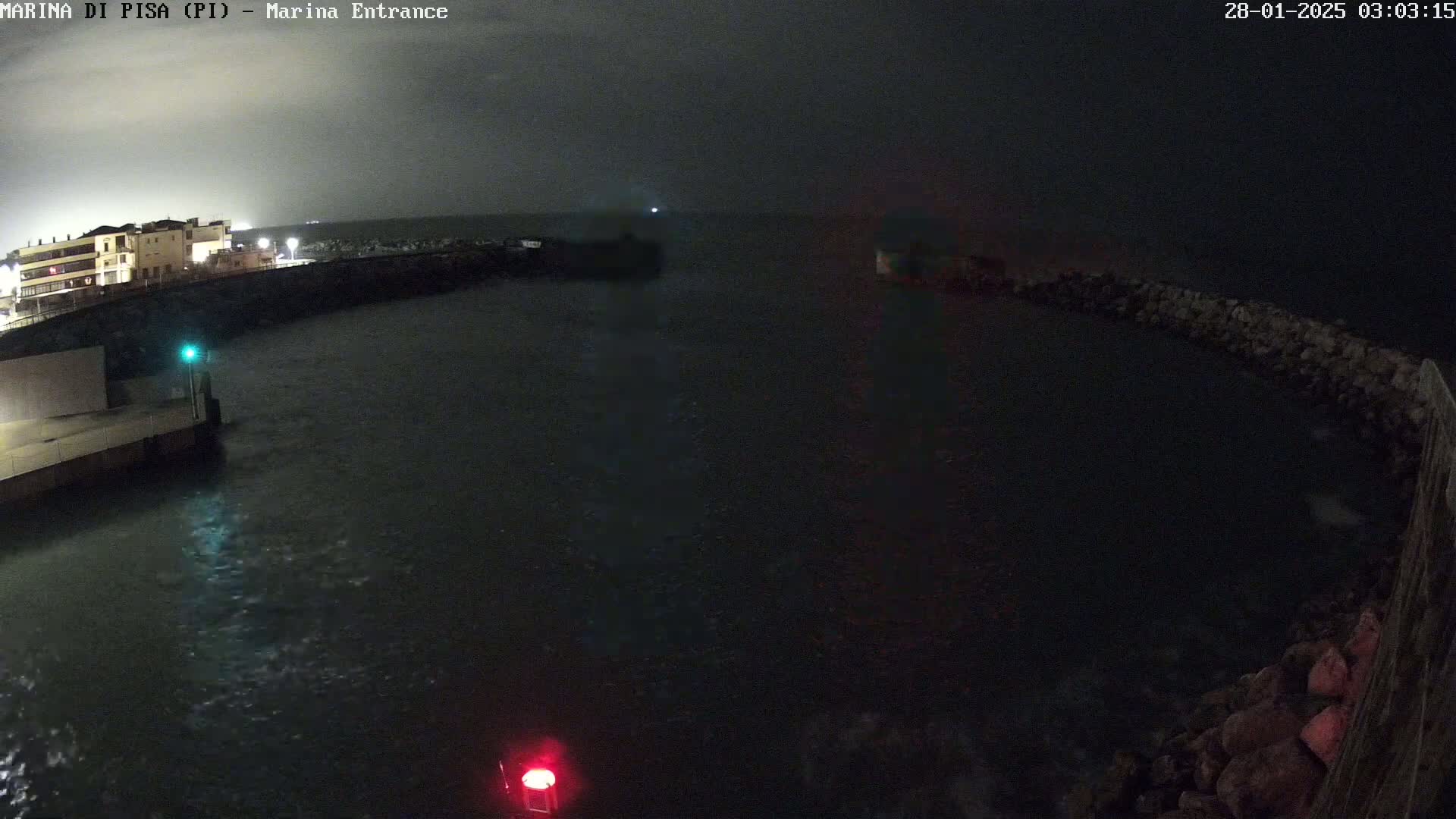 A nighttime view of a dark, choppy harbor with a building on the shore under a cloudy sky.