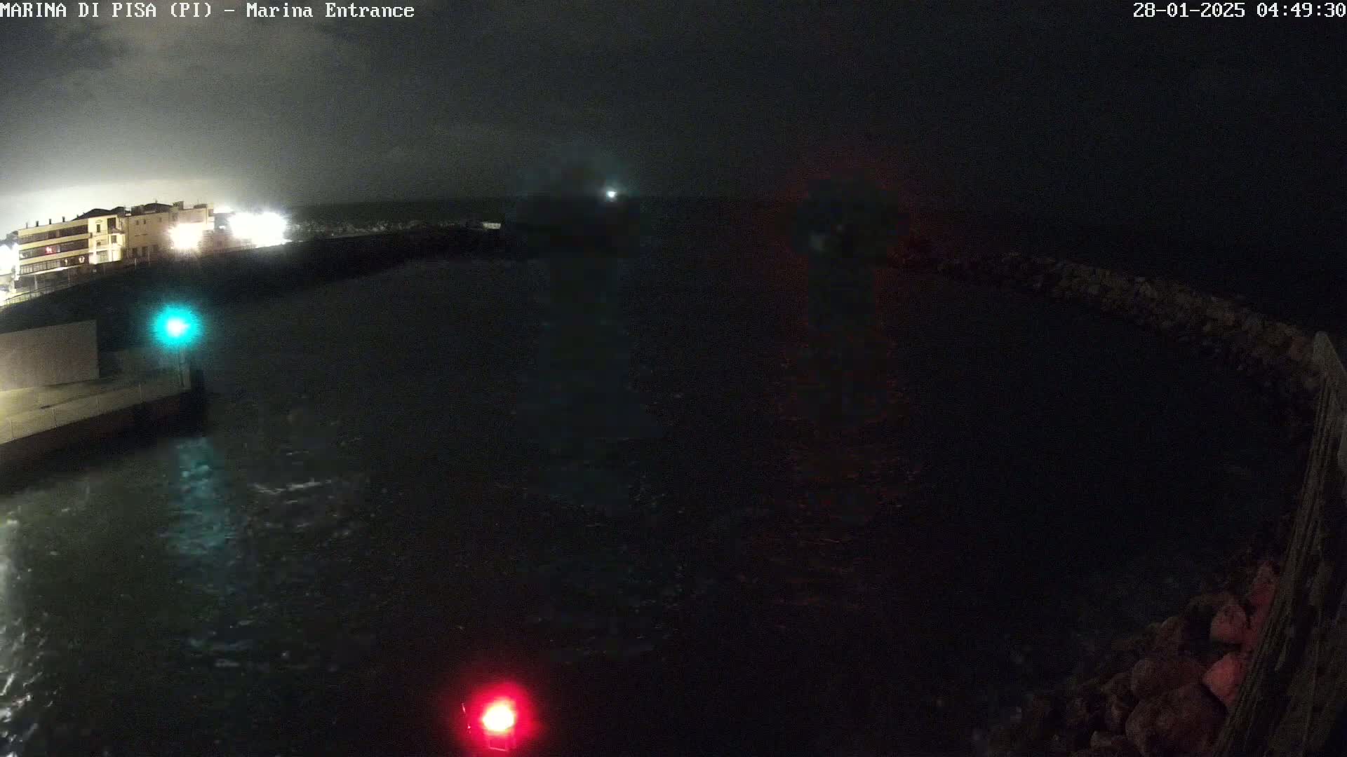 A nighttime view of a marina entrance shows dark, choppy water with a building and lights visible in the background.