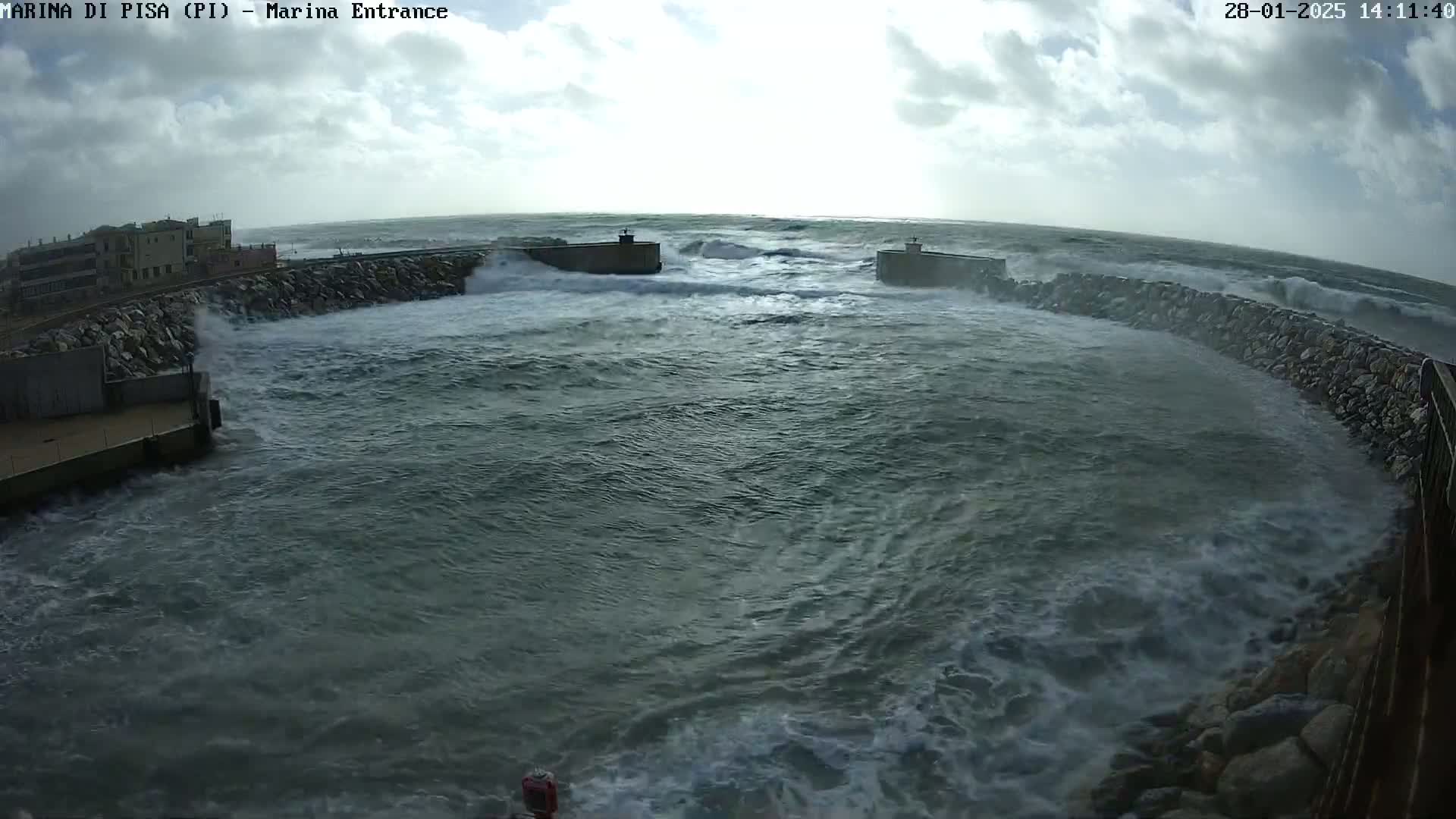 Large waves crash against a stone harbor wall under a cloudy sky.