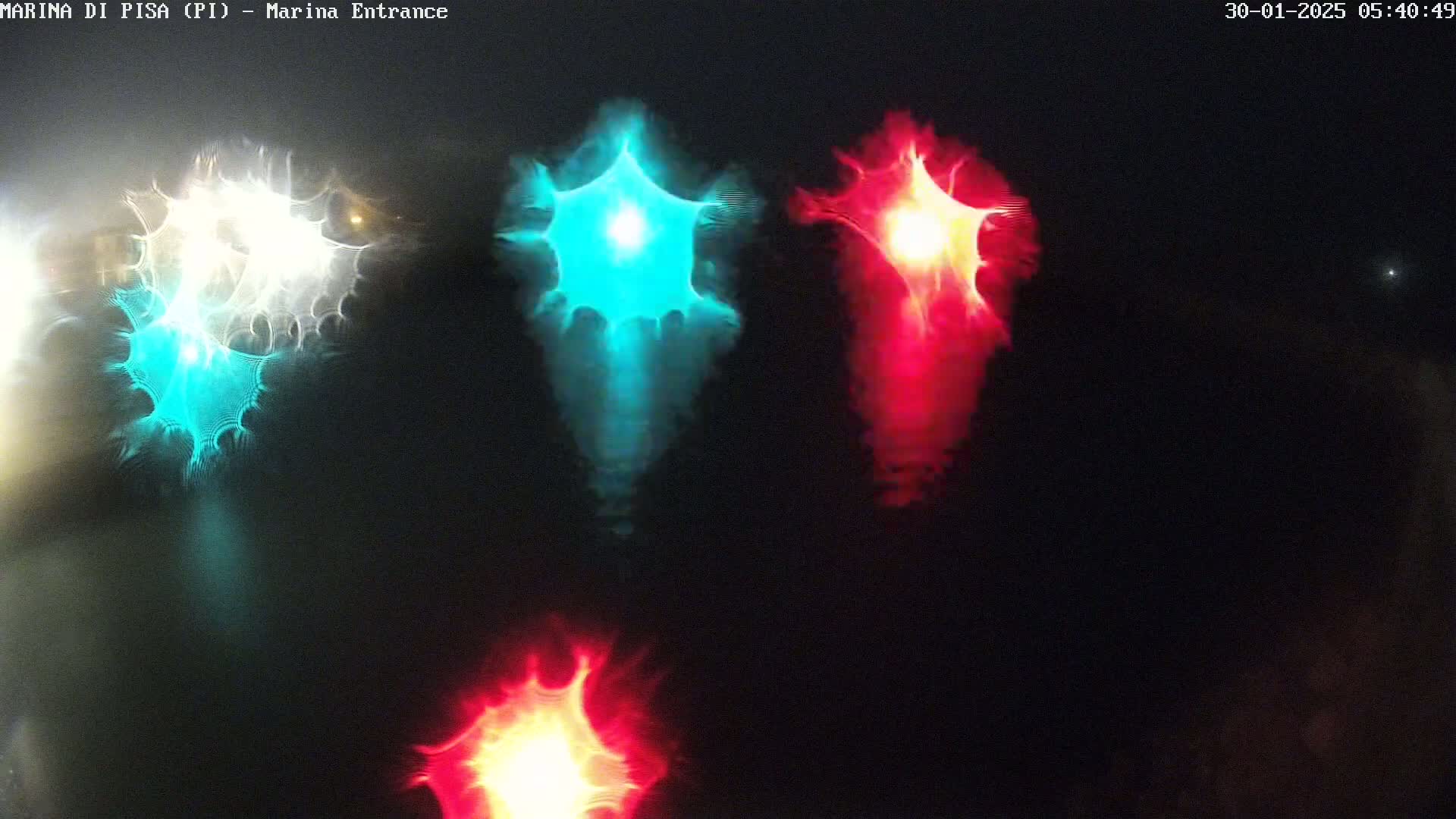Blurred, bright teal, red, and white lights are reflected on a dark, nighttime surface.