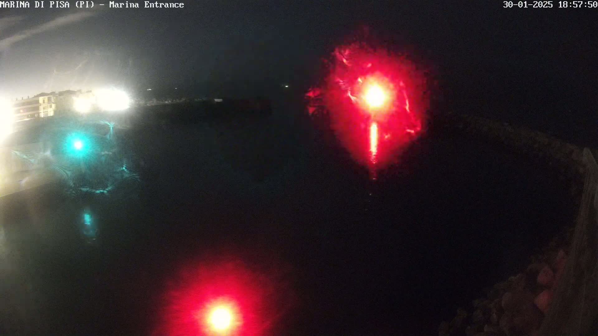 At night, red and green lights illuminate a dark body of water near a shoreline.