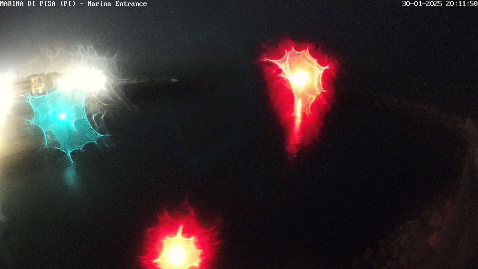 At night, distorted reflections of red and teal lights are seen on dark water.