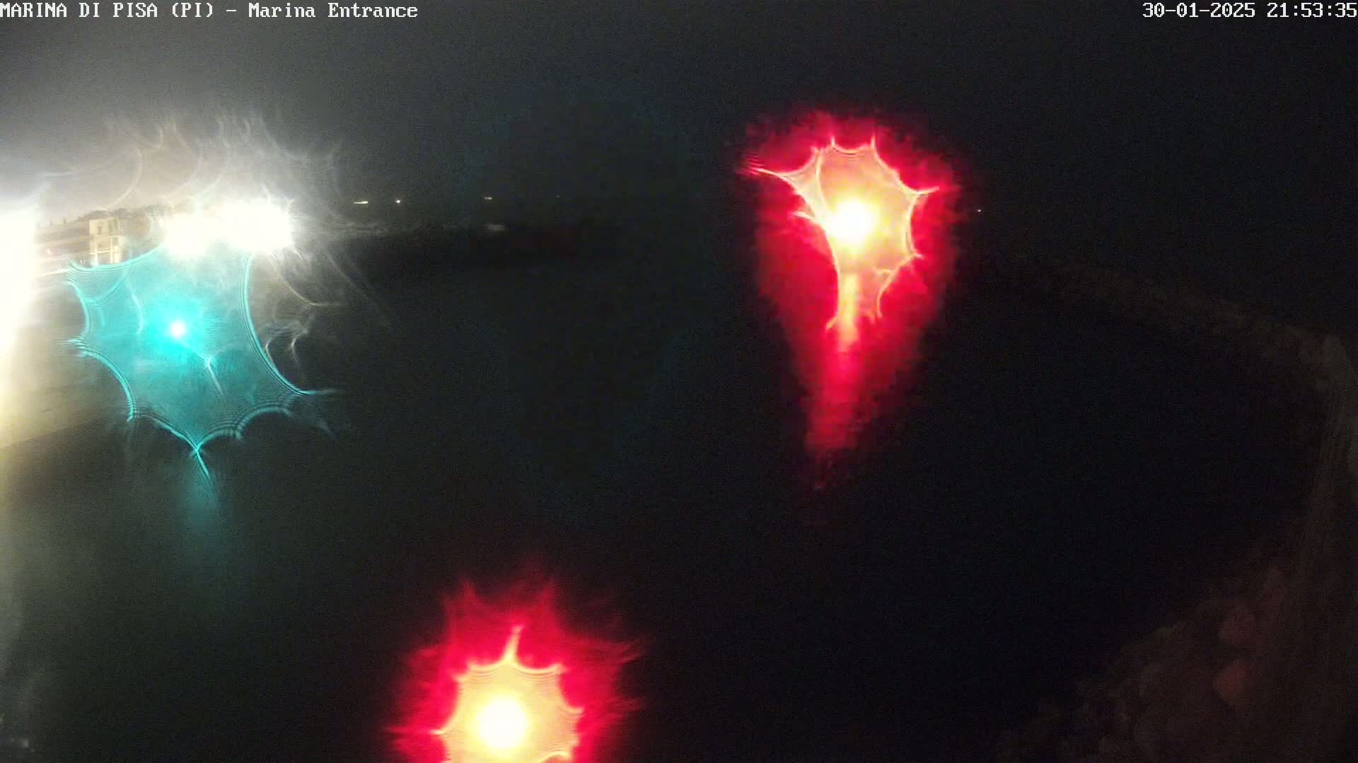 At night, three distorted lights, one teal and two red, are reflected on dark water.